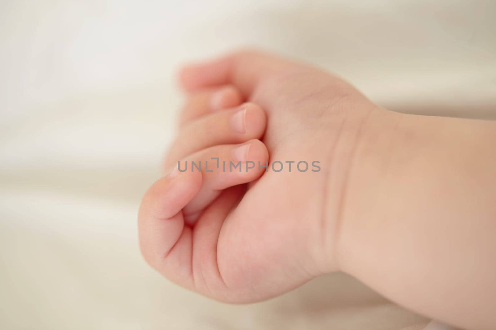 Relax, development and the hand of a baby closeup in a nursery or bedroom of a home for rest at bedtime. Kids, sleeping or wellness with the fist and fingers of a newborn infant child lying on a bed by YuriArcurs