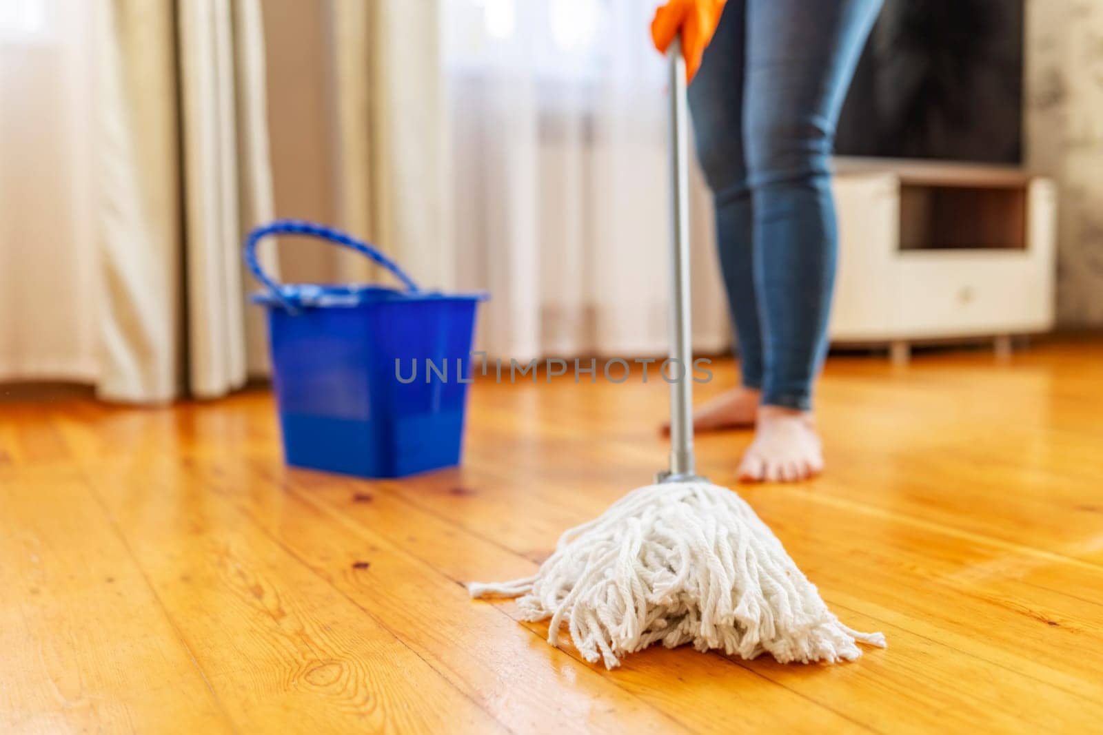 Young woman in protective gloves washing a wooden floor with a mop, doing homework, routine cleaning, cleaning job concept