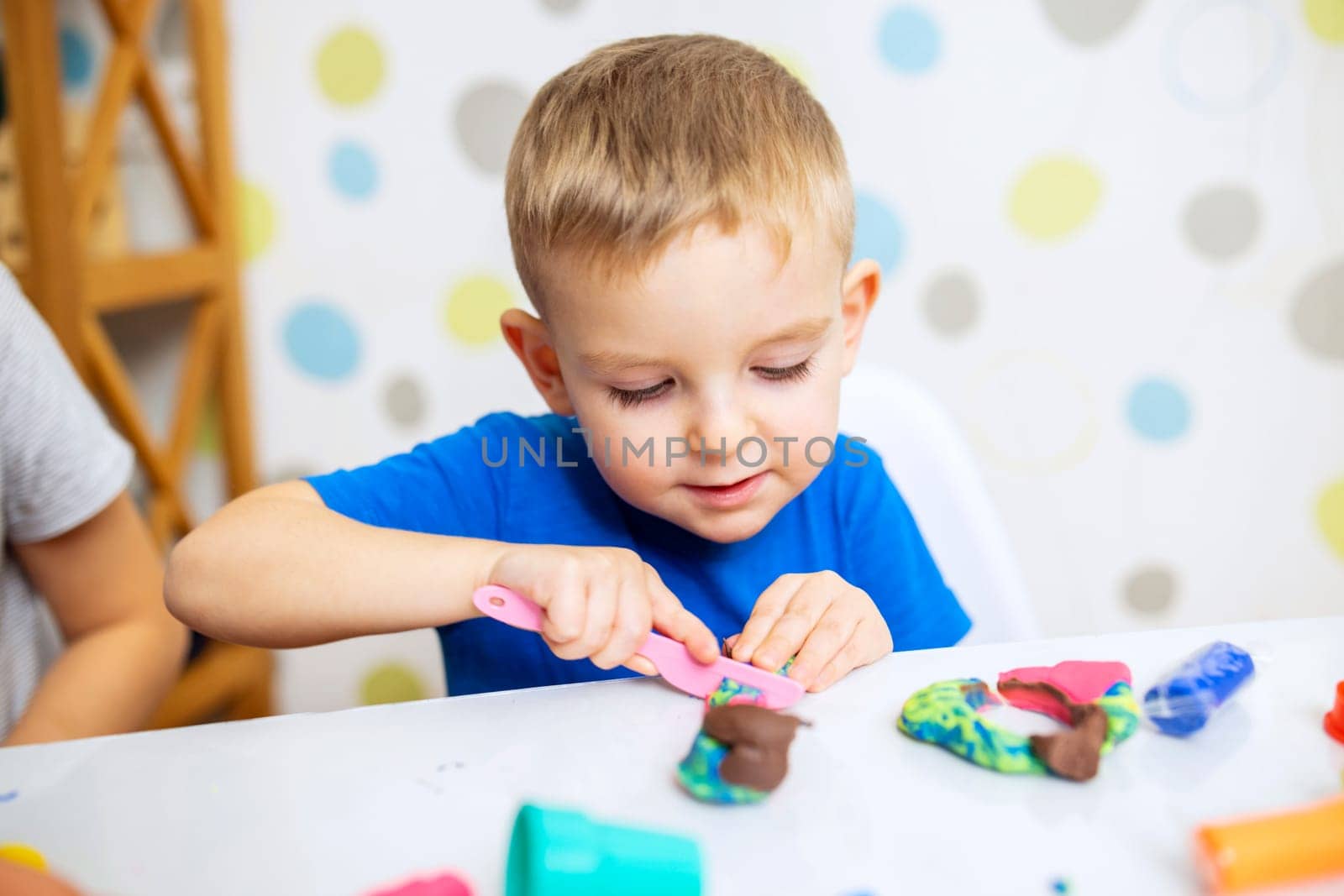 Little boy enthusiastically plays with plasticine, play dough on white table by andreyz