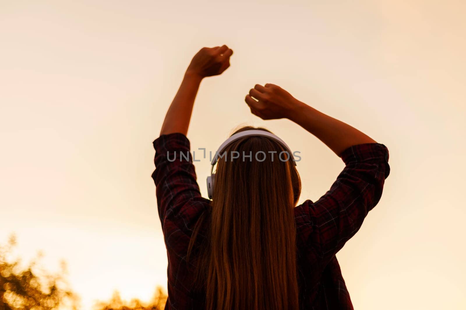 Silhouette of young woman in headphones enjoying music and dancing at sunset by andreyz
