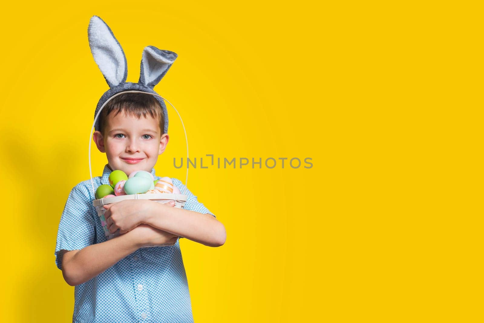 Cute little child is wearing bunny ears on Easter day and holding basket with painted eggs. Happy kid is holding Easter basket.
