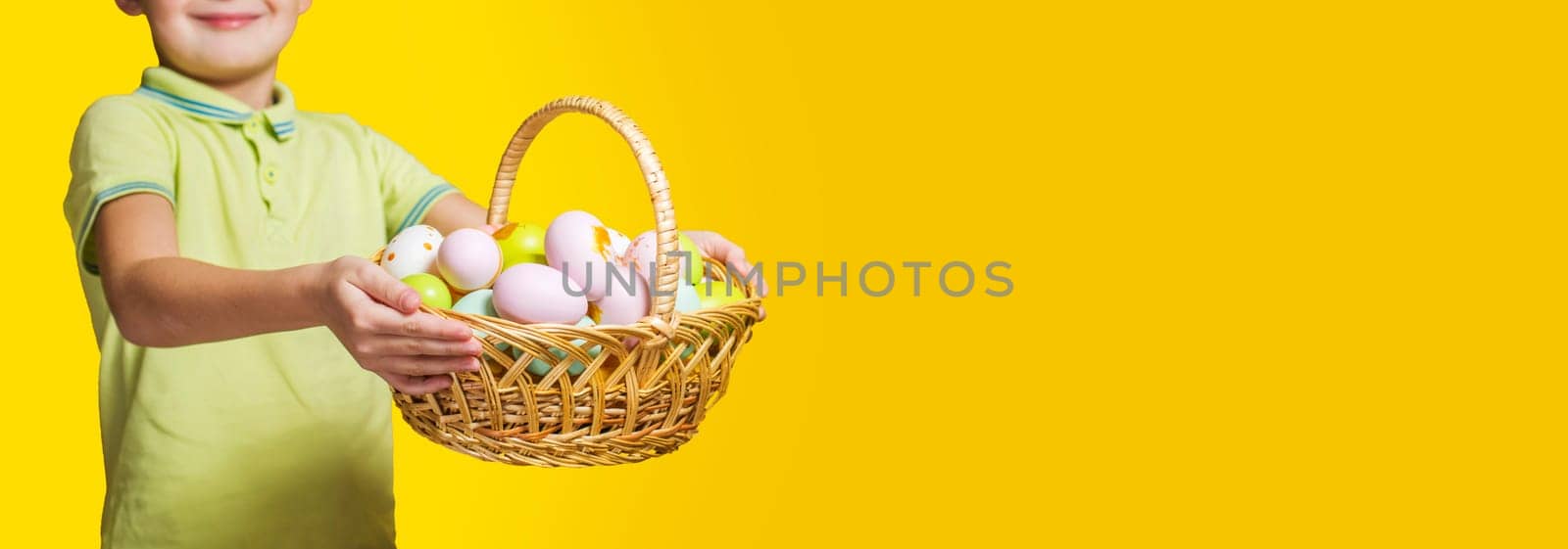 Little child is holding basket with painted eggs on yellow background. Easter day.