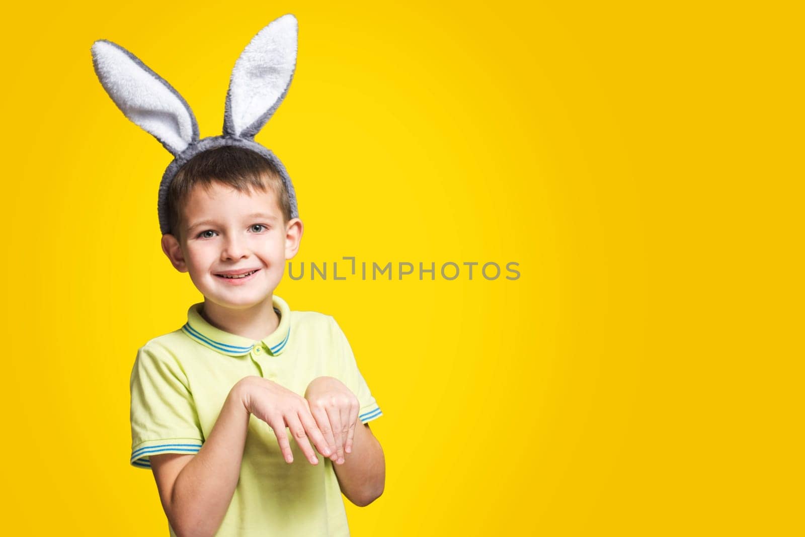 Portrait of a smiling adorable little boy wearing bunny ears on a yellow background.