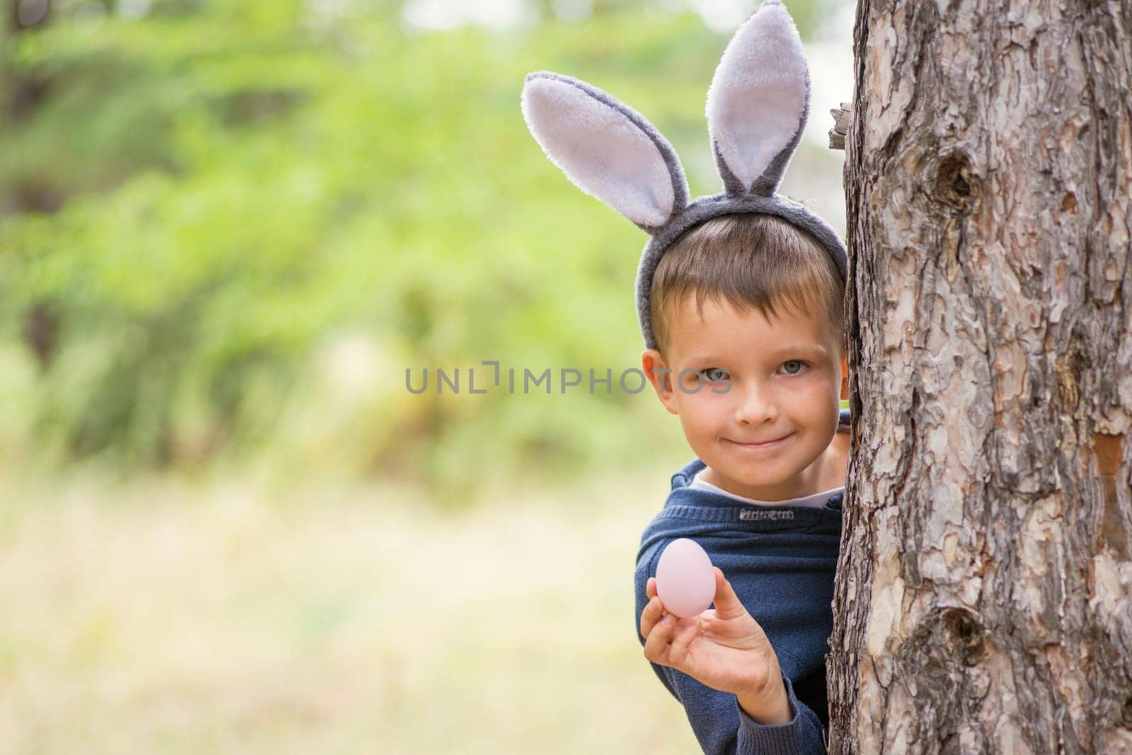 Cute little boy with rabbit ears holding easter egg on green natural background. Egg hunt at spring time. Happy Easter day.