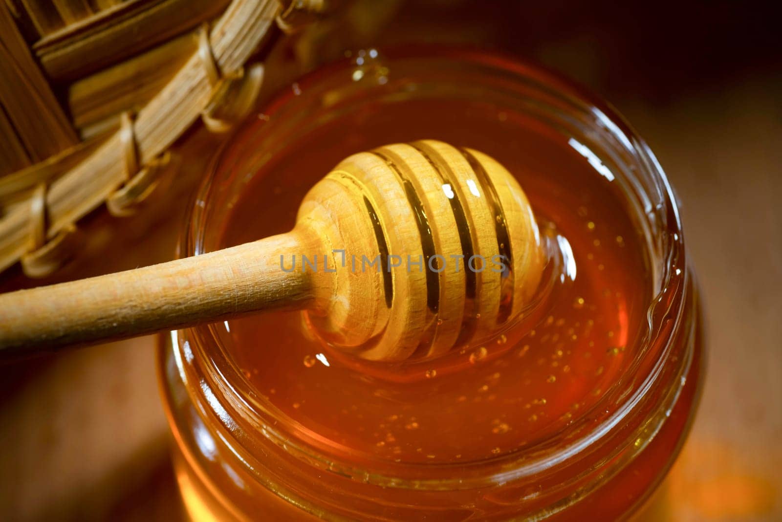 Liquid honey with a honey dipper in a glass jar on a wooden table. Healthy organic honey. Close-up, side view.