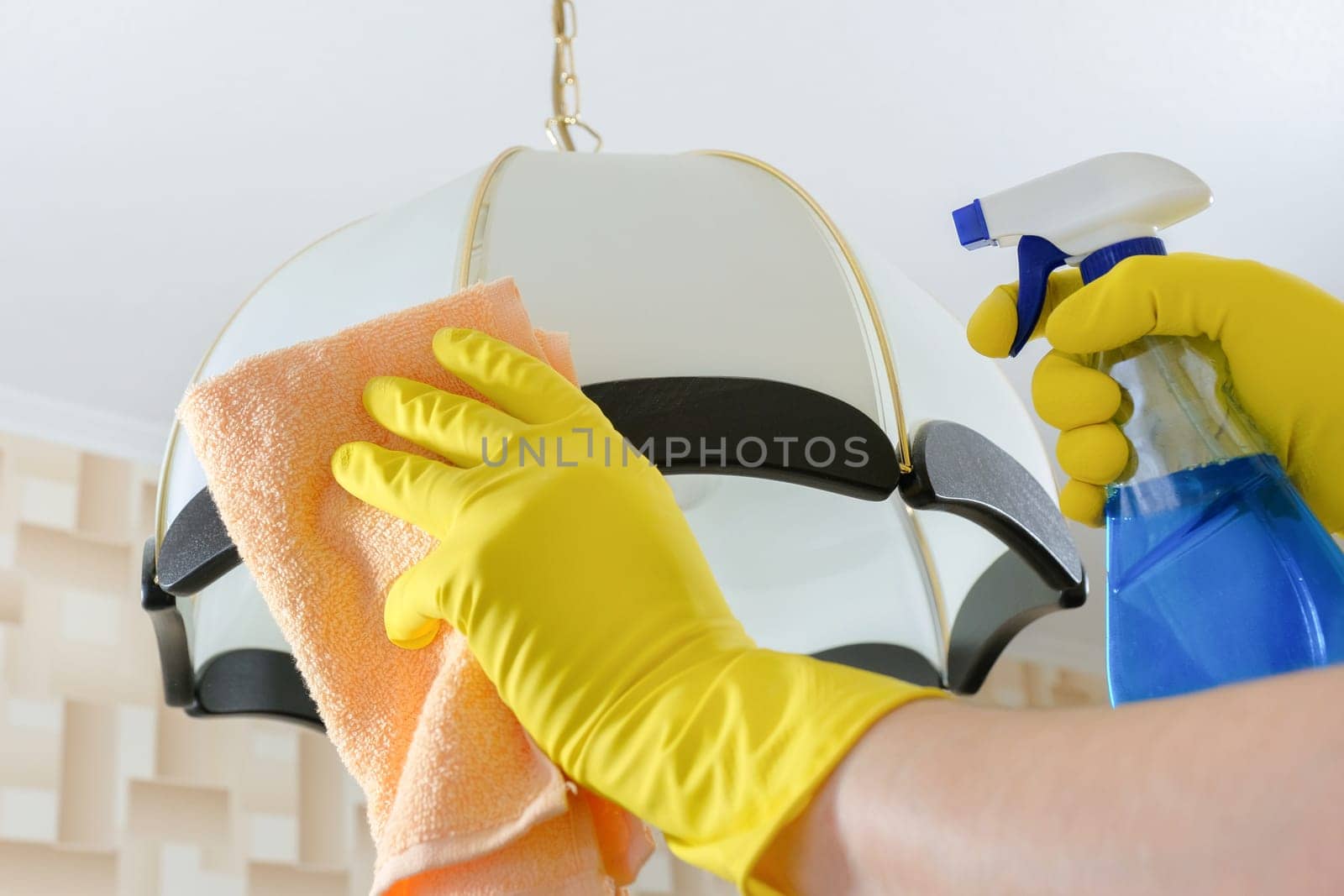 The cleaner wipes the dust from the chandelier with a rag and detergent. Cleaning service by Shablovskyistock