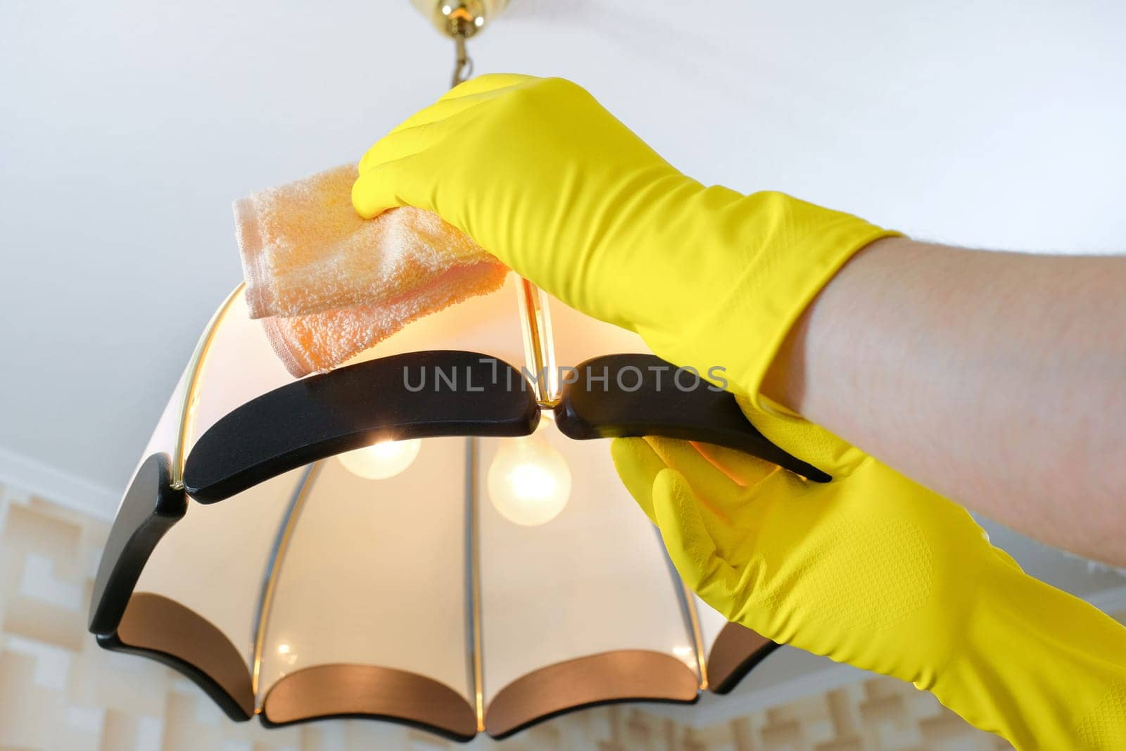 The cleaner wipes the dust from the chandelier. House cleaning by Shablovskyistock
