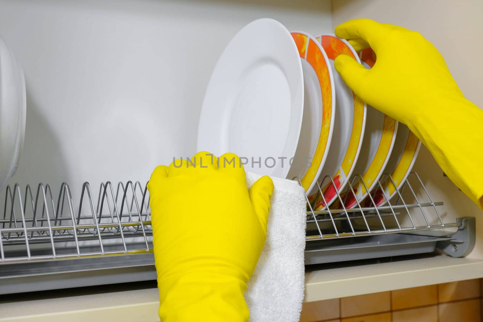 Hands in rubber gloves wipe dishes in the kitchen. House cleaning.