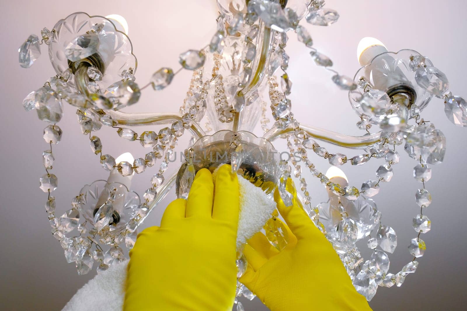 Close-up of gloved hands wipes dust from the chandelier. House cleaning by Shablovskyistock