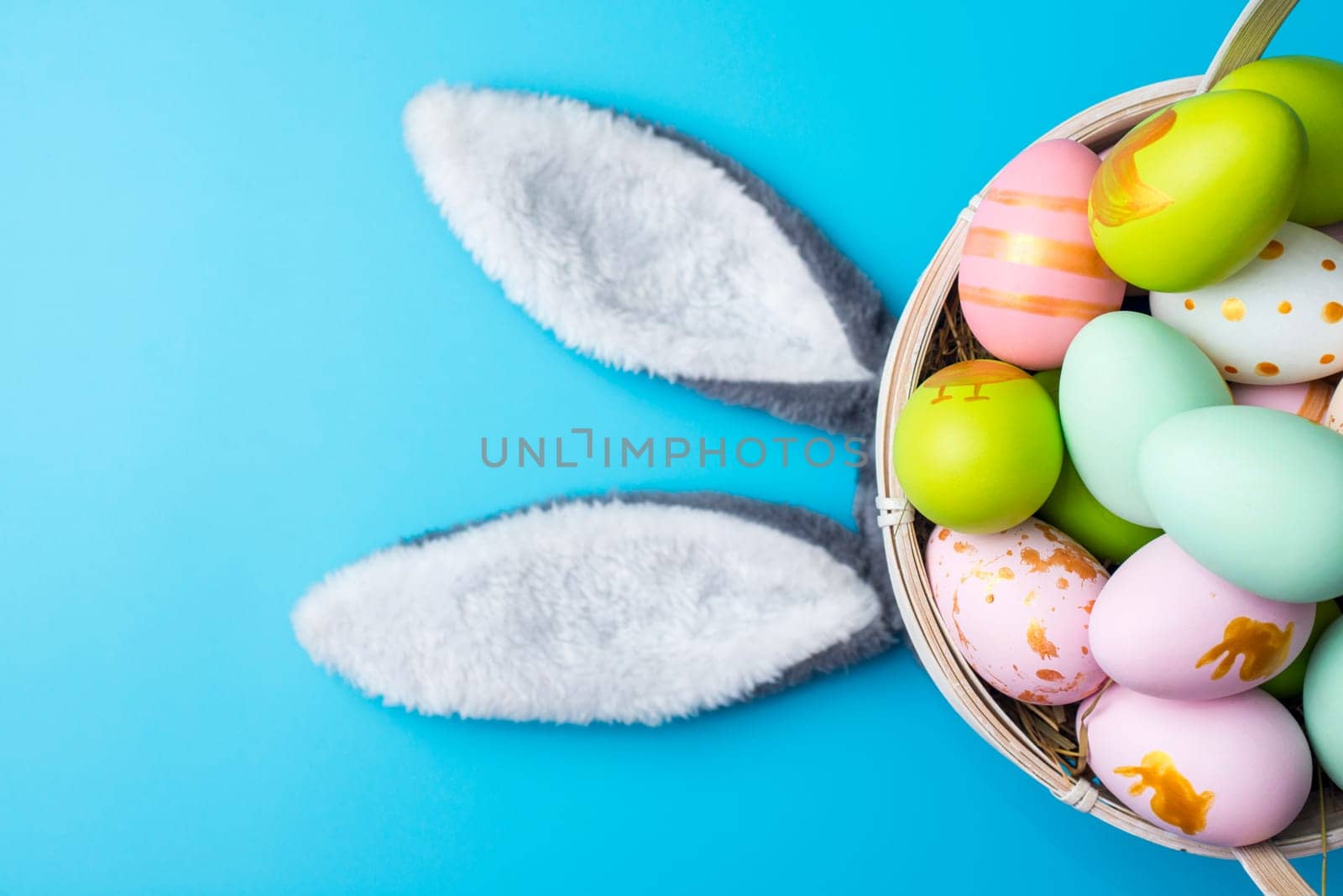 A basket of Easter eggs with bunny ears on blue background. Top view. Easter greeting card.