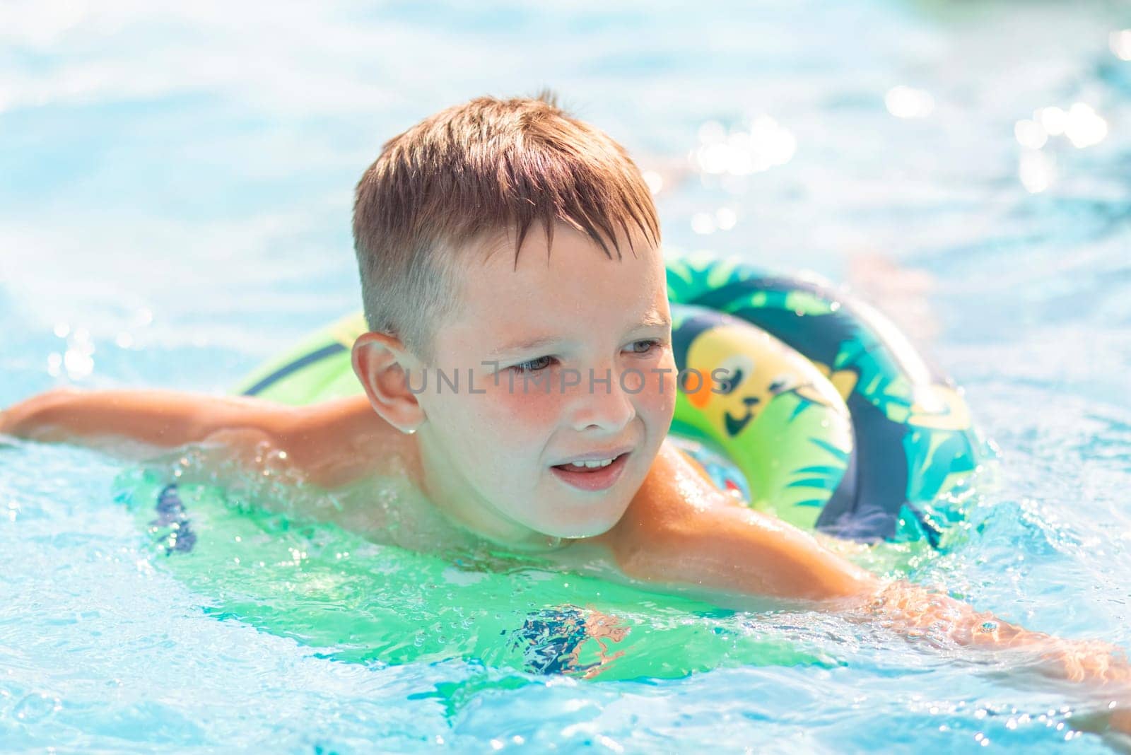 Funny happy child boy in swimming pool on inflatable rubber circle ring. Kid playing in pool. Summer holidays and vacation concept.