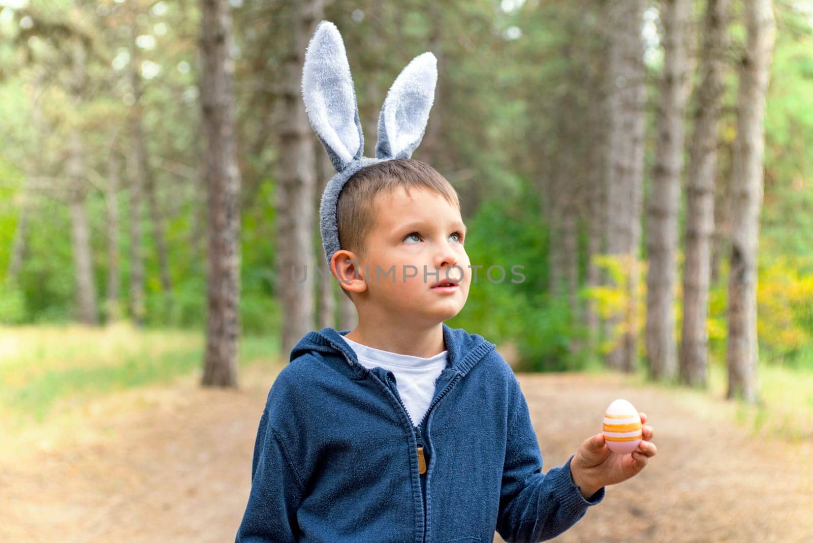 A child looking for Easter eggs in the forest. Little boy hunting for Easter egg in spring wood on Easter day. The concept of Easter Egg Hunt.