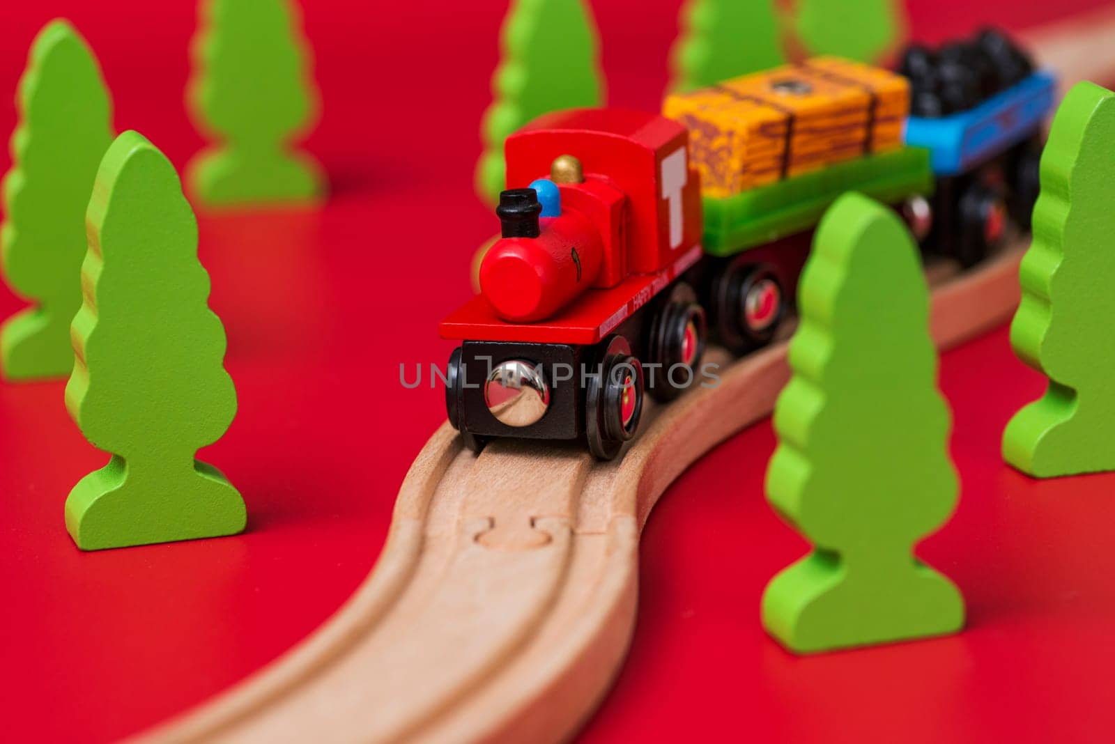 Wooden toy train on the railroad among green trees on red background. Educational toys for preschool and kindergarten child.