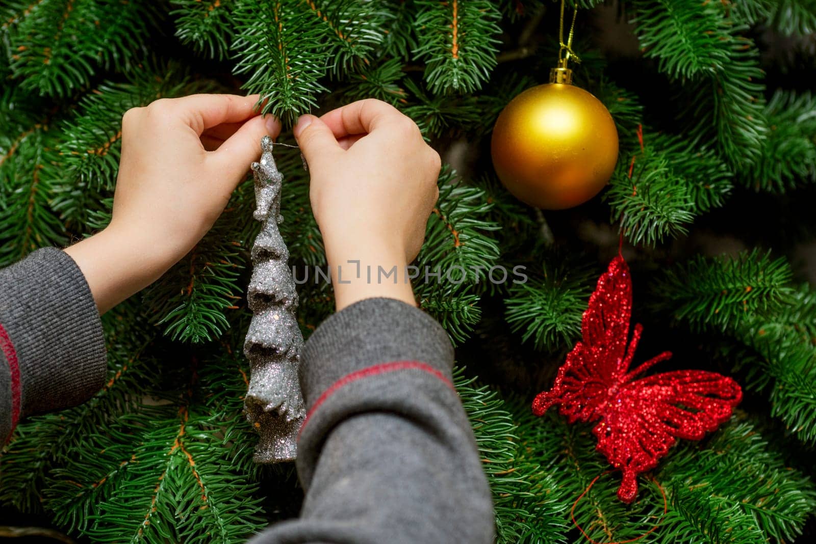 Little kid is decorating Christmas Tree with toys and baubles. Cute kid preparing home for xmas celebration.