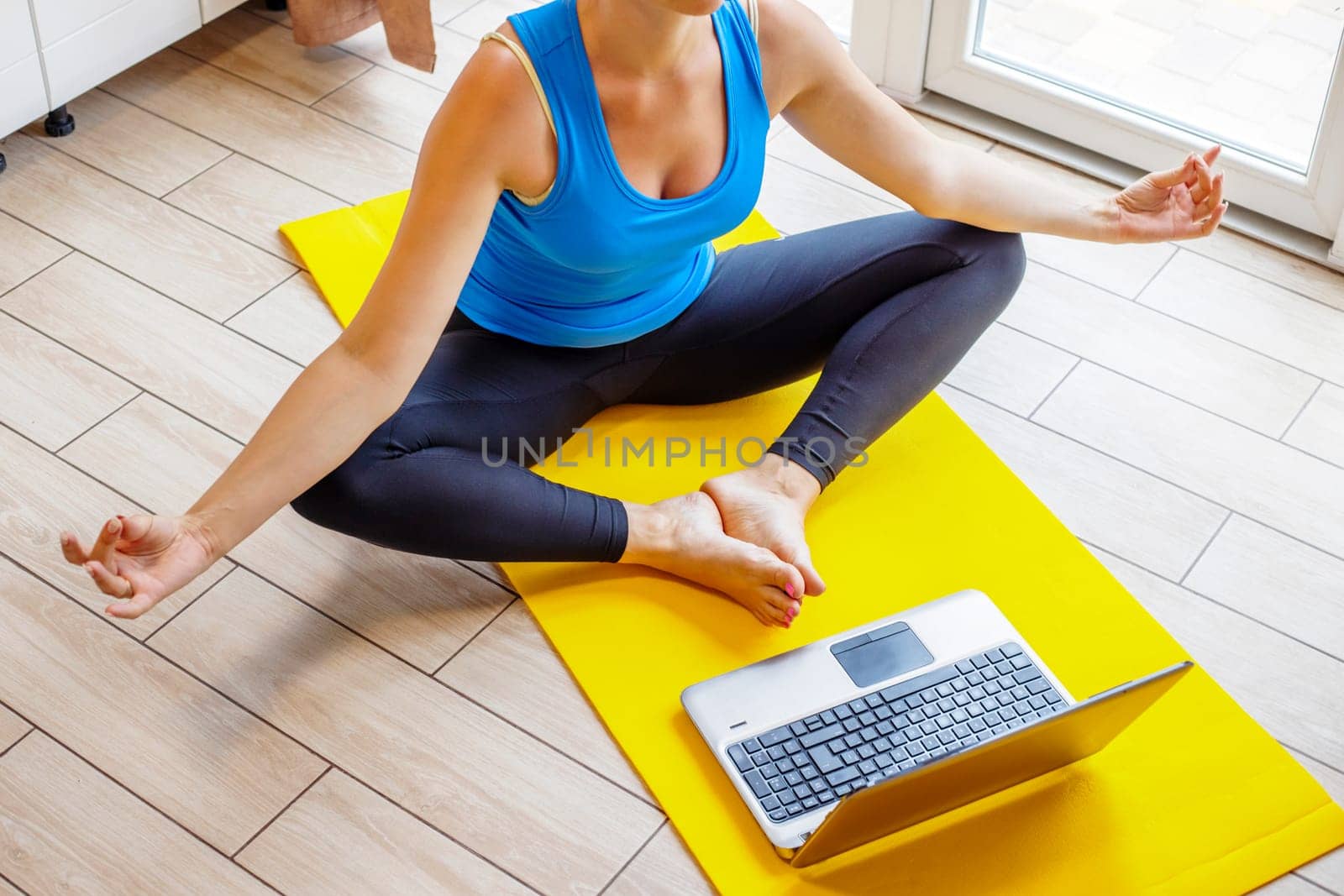 Yoga online. Young sporty slim woman in sportswear practicing meditation with laptop at home, sitting in lotus position in front of computer on floor.