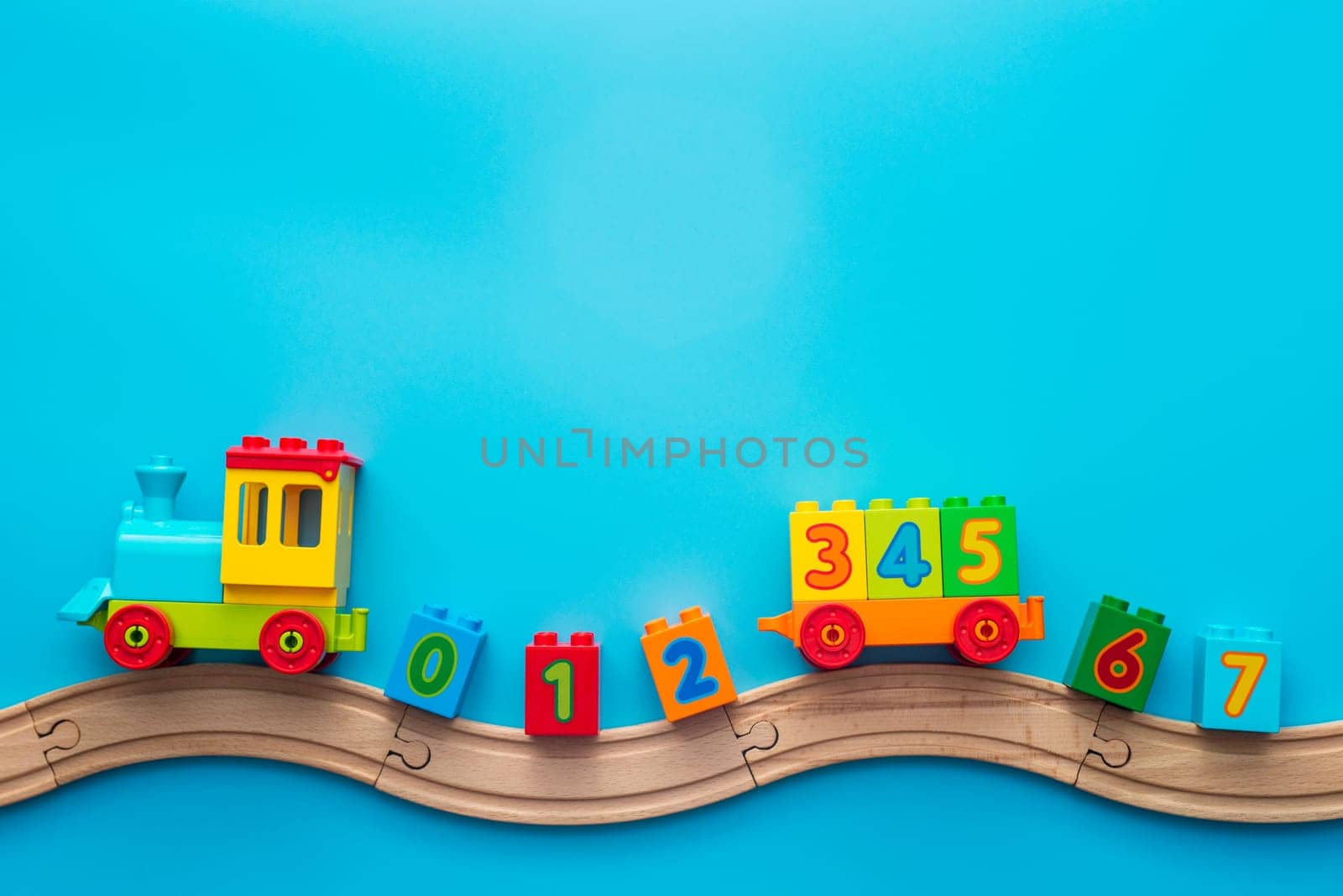 Colorful toy train locomotive with numbers on wooden railway on blue background. Kids toys background banner. Early childhood education, learning to count, preschool and kids game concept.