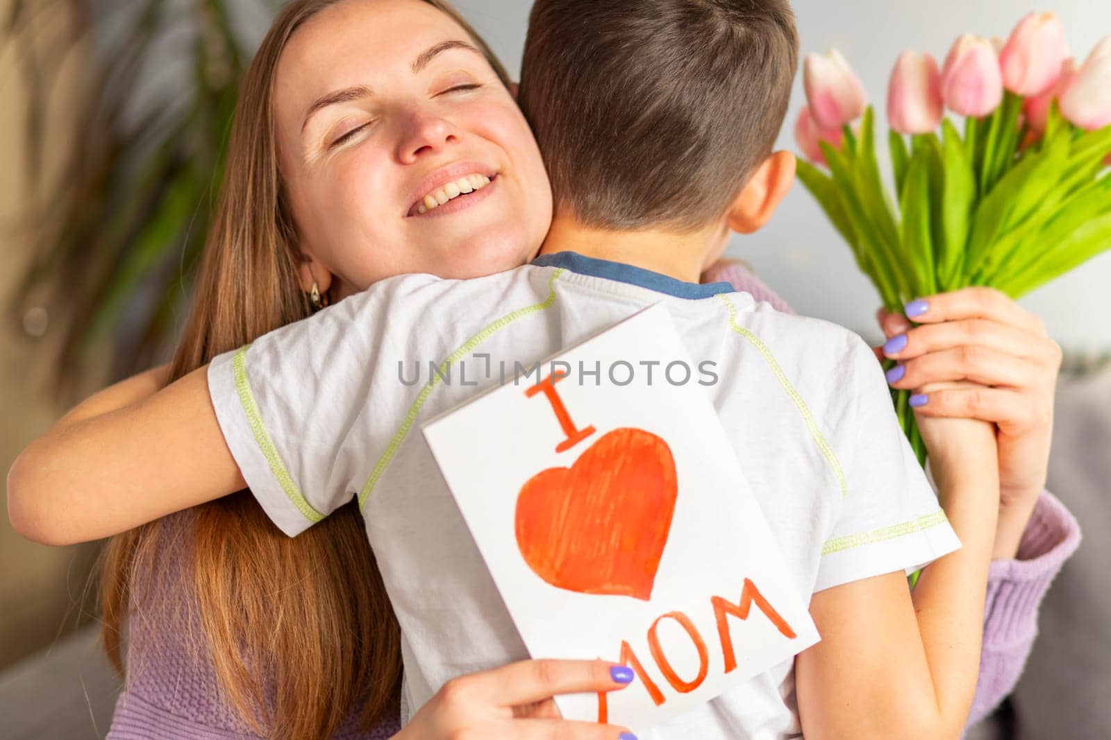 Happy mother's day. Child son congratulates his mother and gives her a postcard and a bouquet of tulips.