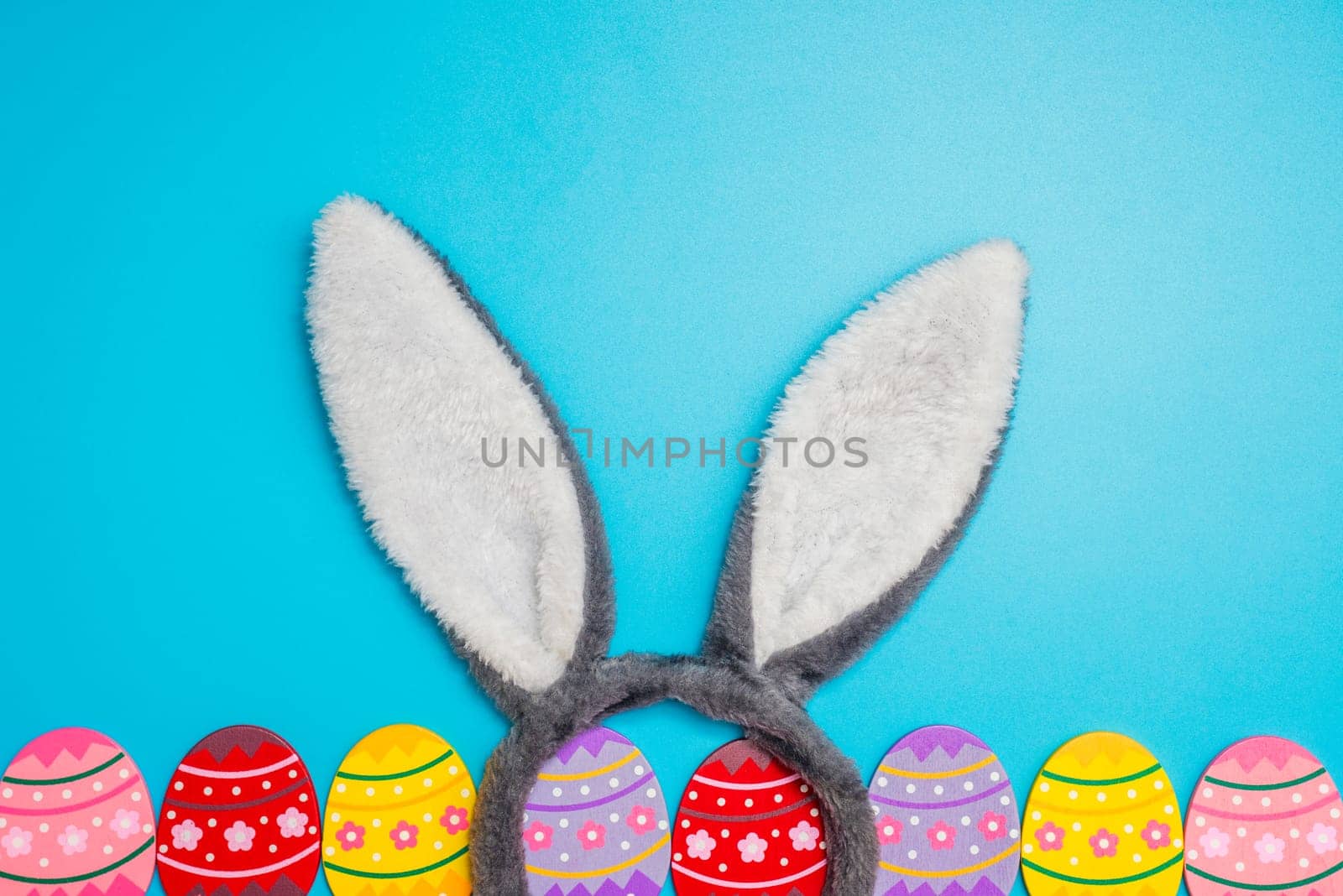 Colorful painted Easter eggs with bunny ears on blue background. Top view. Easter greeting card.