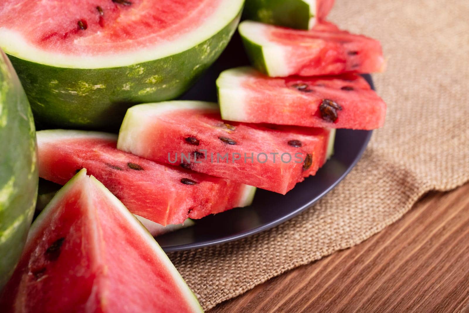 Fresh red watermelon pieces on a black plate on a wooden table. Sweet and juicy watermelon.