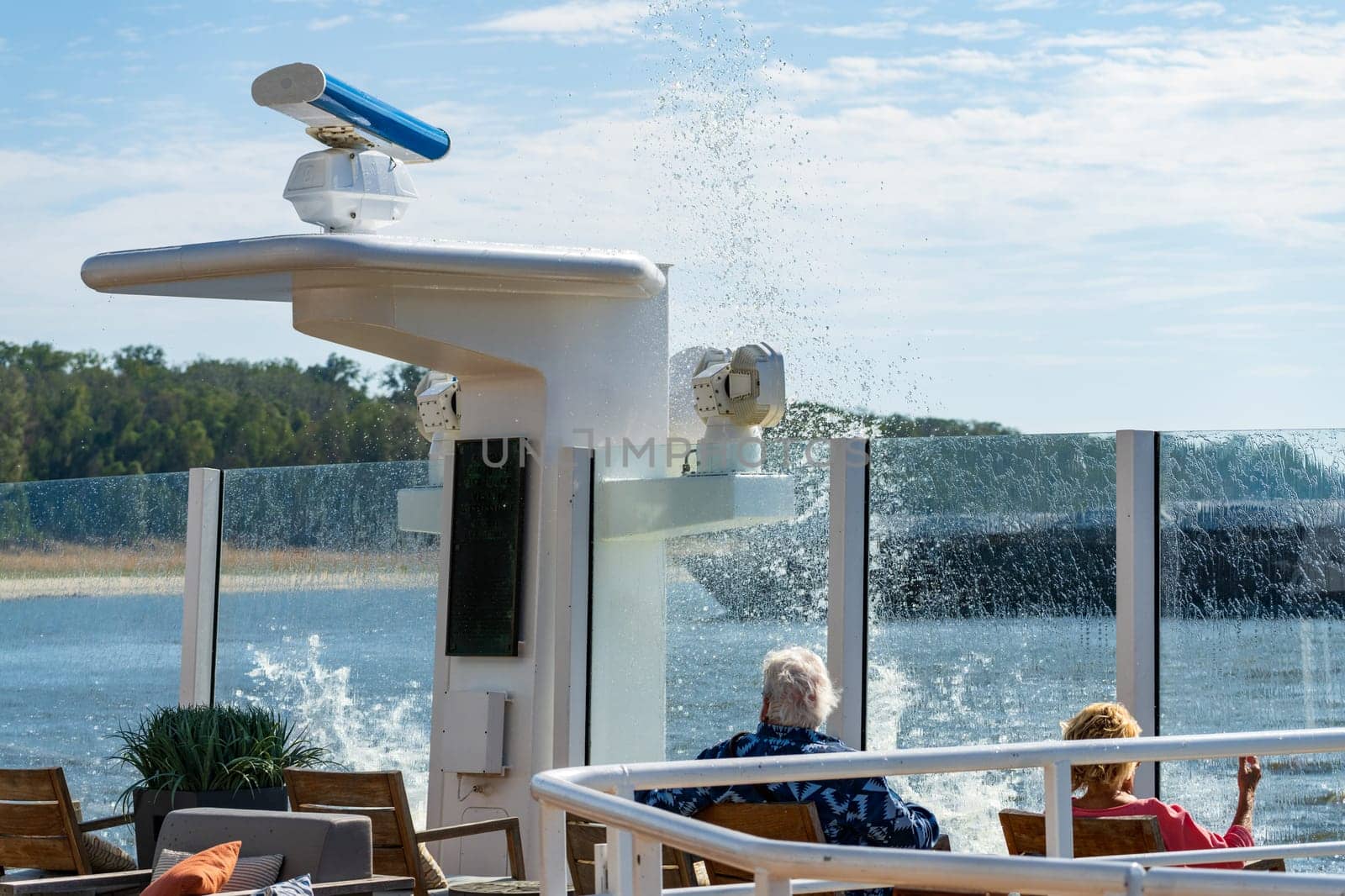 Spray and wave from passing freight barge creates splash onto deck of a modern Mississippi river cruise boat