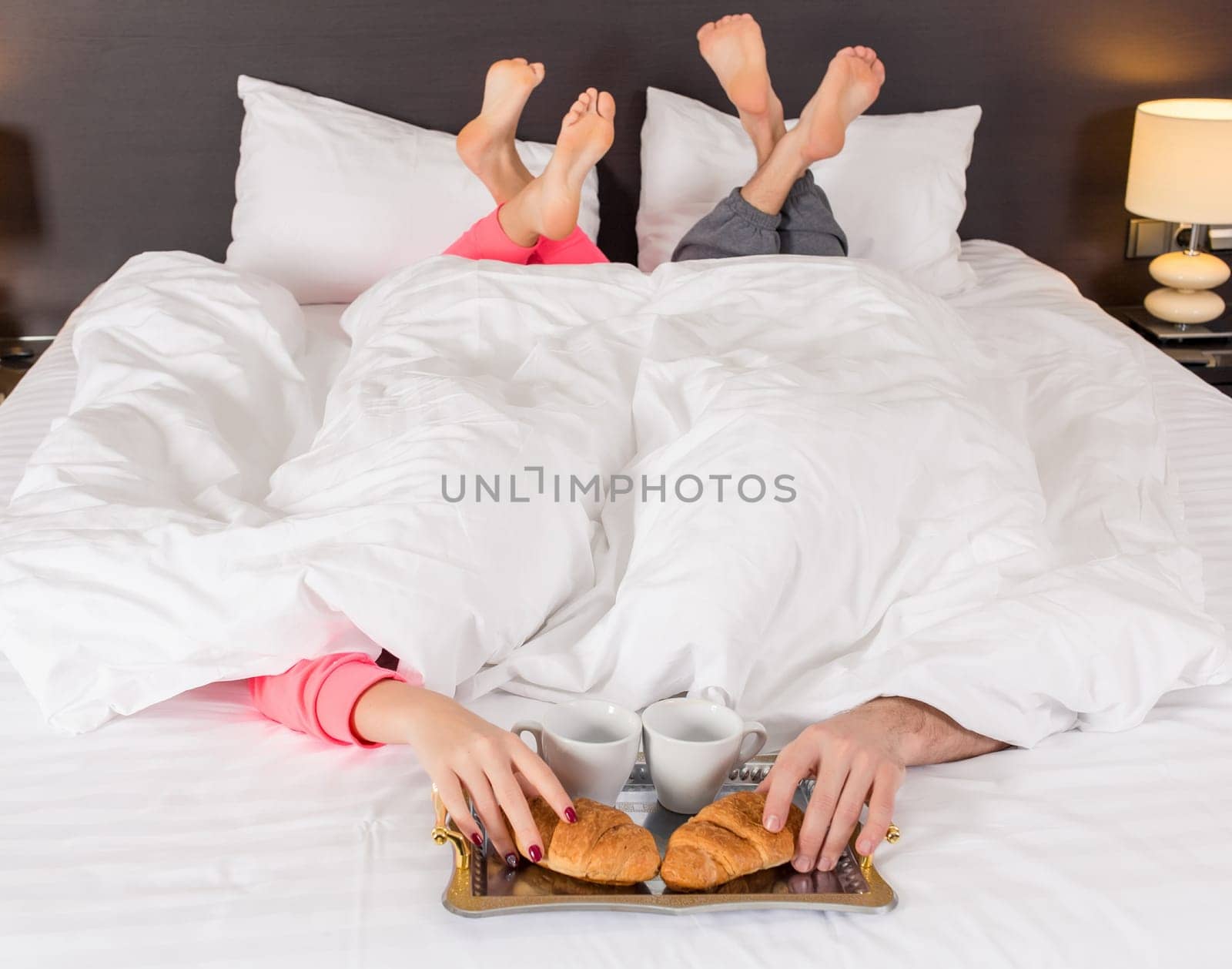 Happy young couple having breakfast tray on bed at home in bedroom. Young couple drink coffee in bed, happy smile woman man lovers