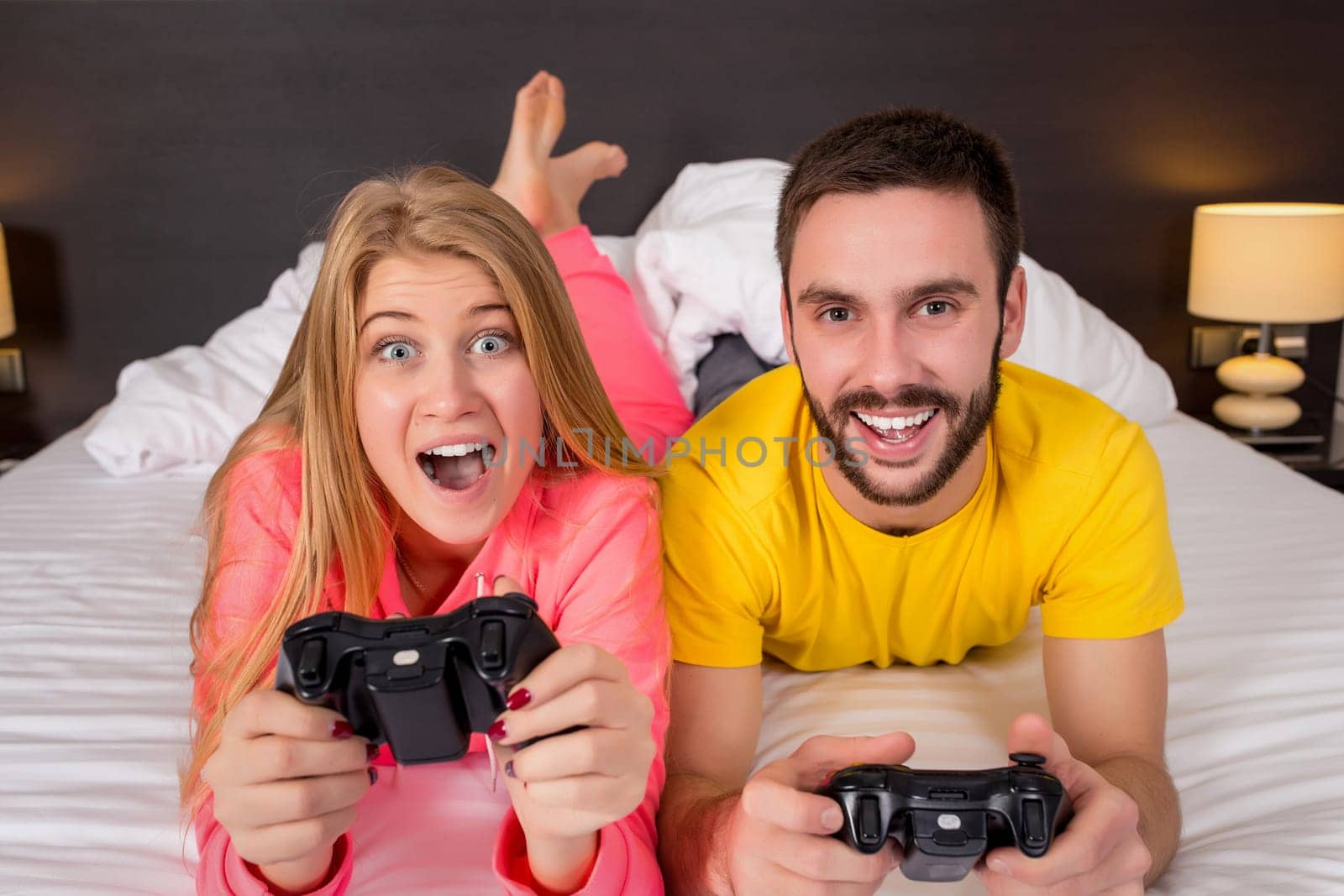 Happy young couple having fun playing videogames in bed.