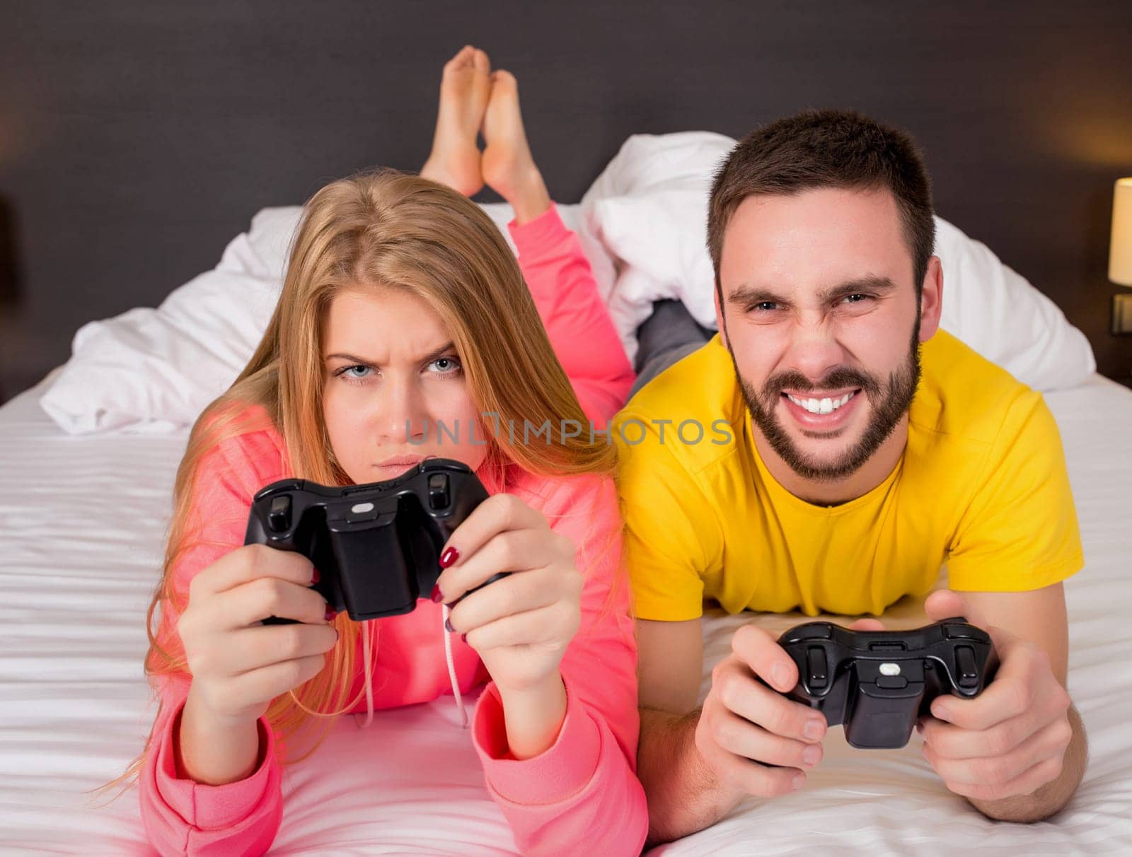 Happy young couple having fun playing videogames in bed.