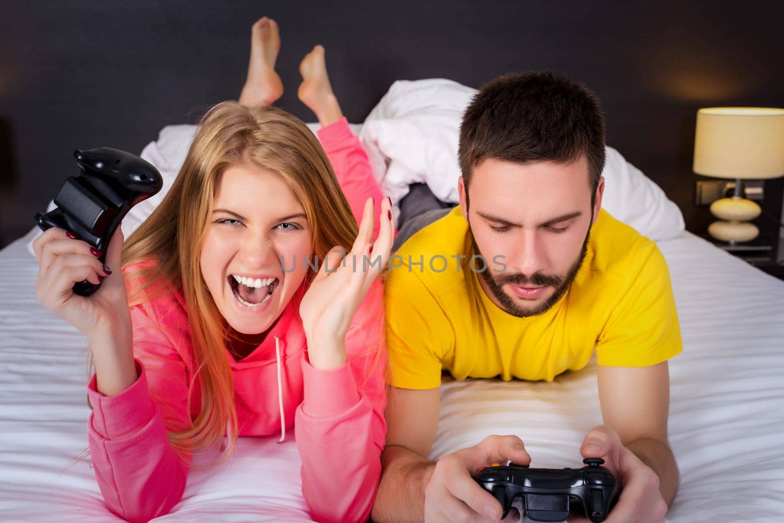 Young couple having fun playing videogames in bed.