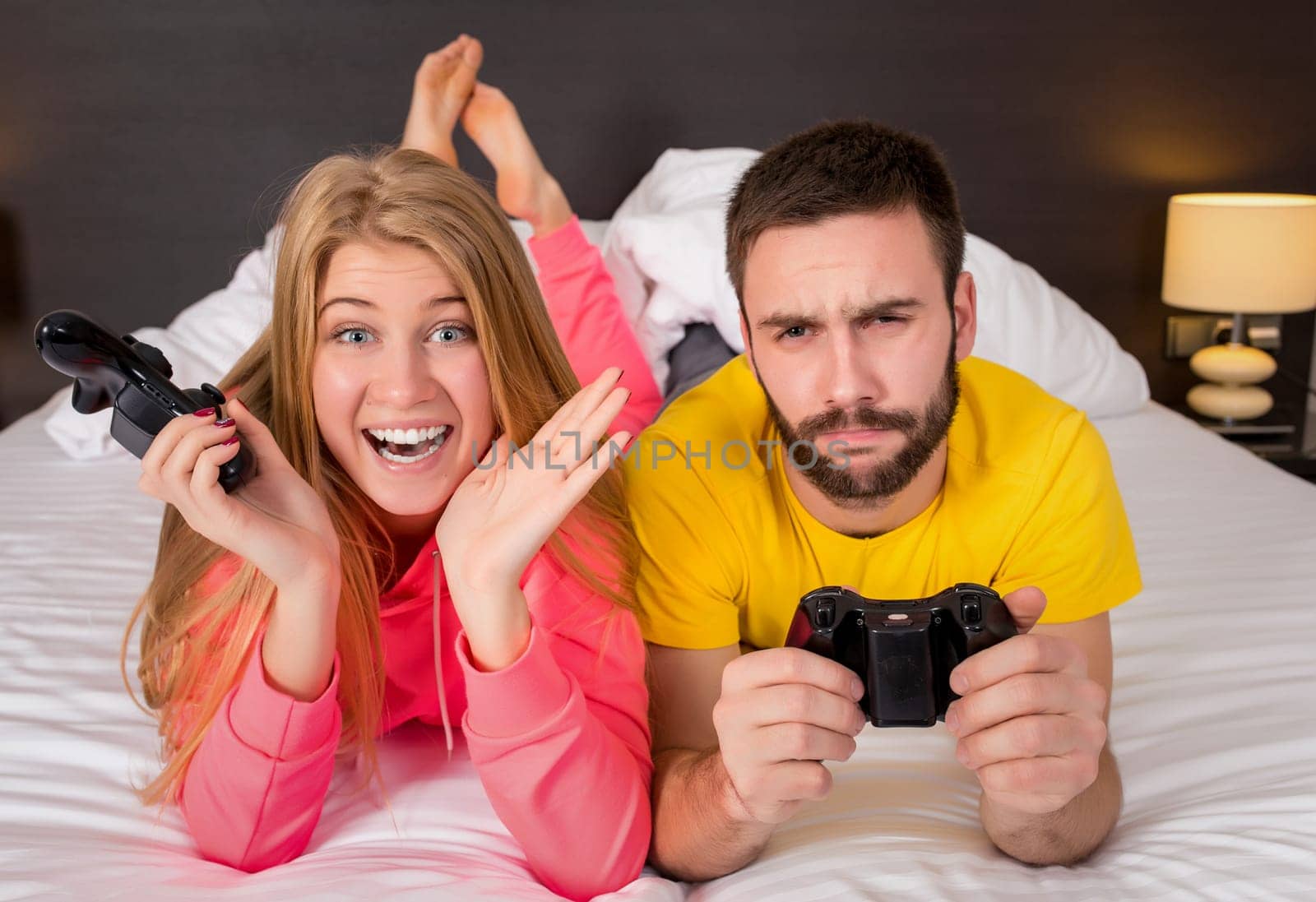 Happy young couple having fun playing videogames in bed.