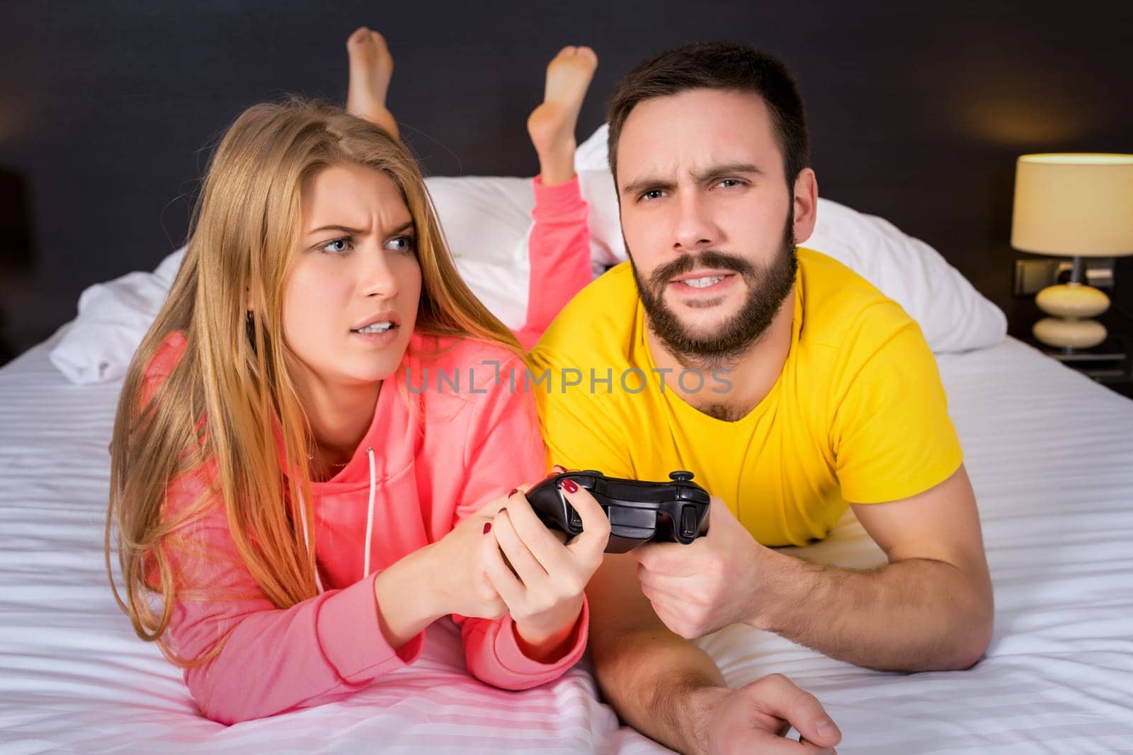 Young couple having playing videogames in bed. Guy playing a video game, she complains that she did not pay attention