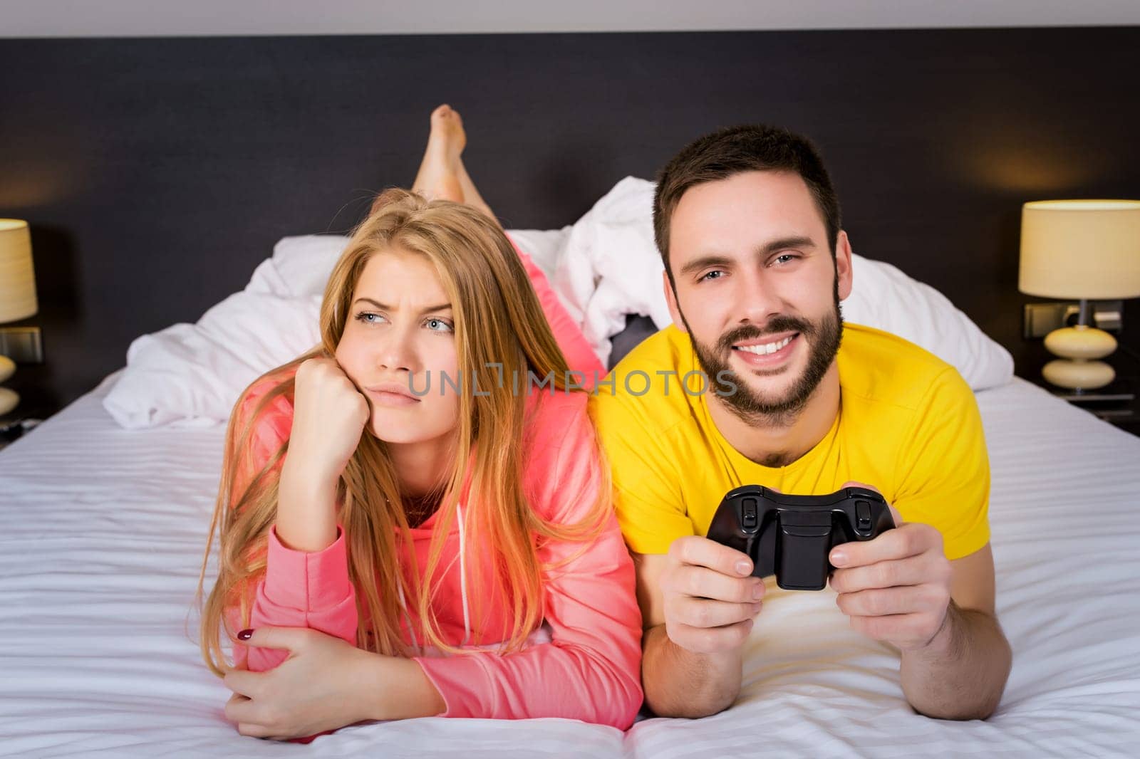 Young couple having playing videogames in bed. Man playing video game, woman upset.