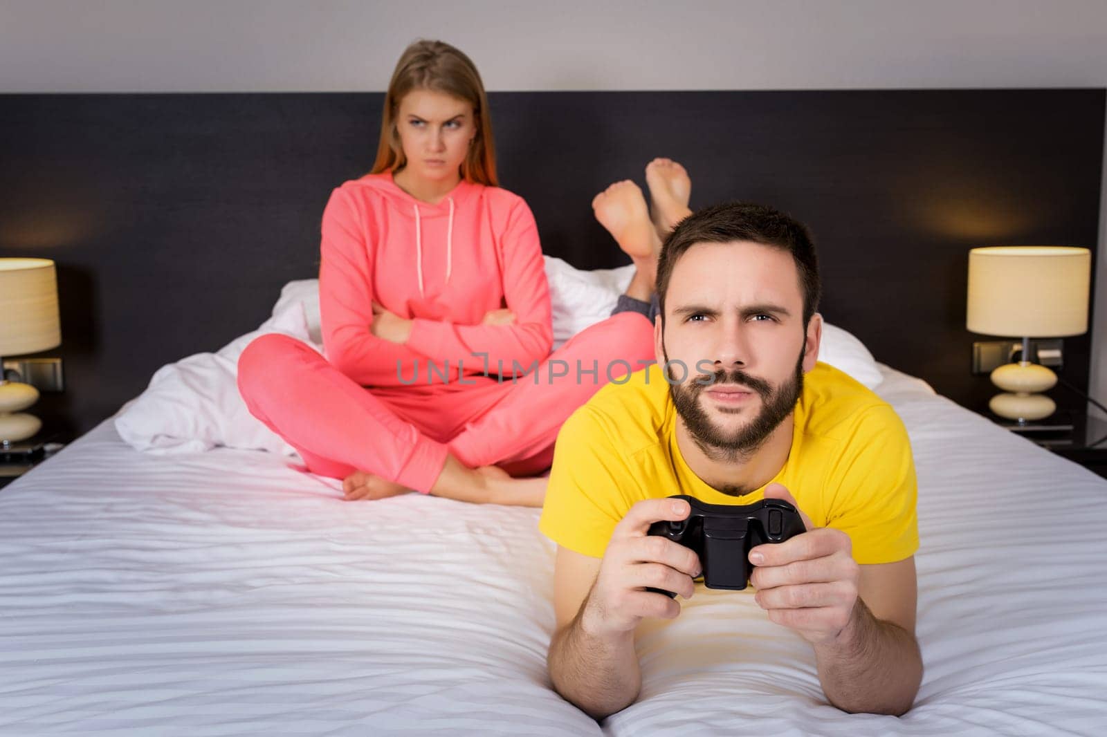 Young couple having playing videogames in bed. Man playing video game, upset woman on background.