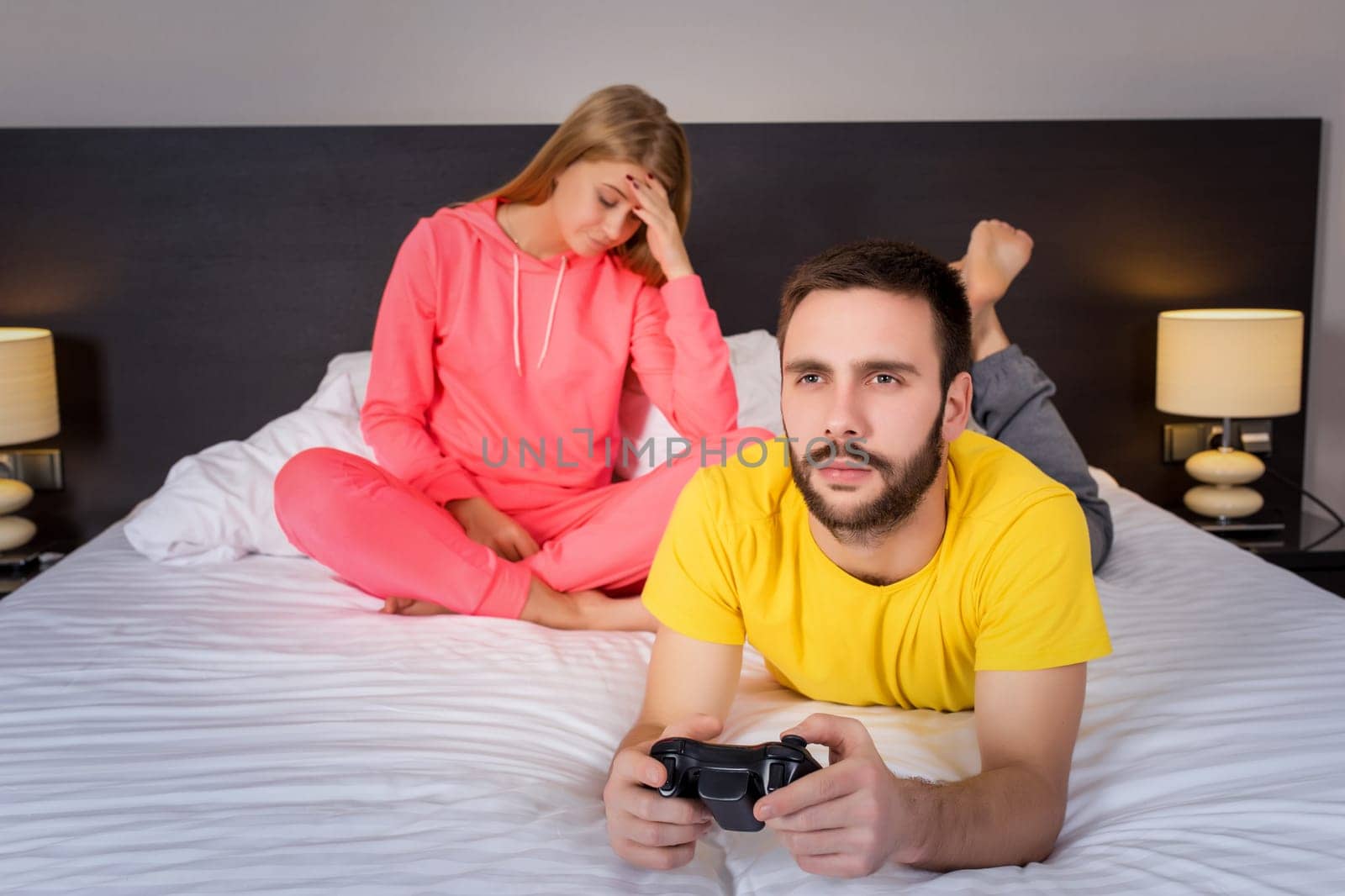 Young couple having playing videogames in bed. Man playing video game, upset woman on background.
