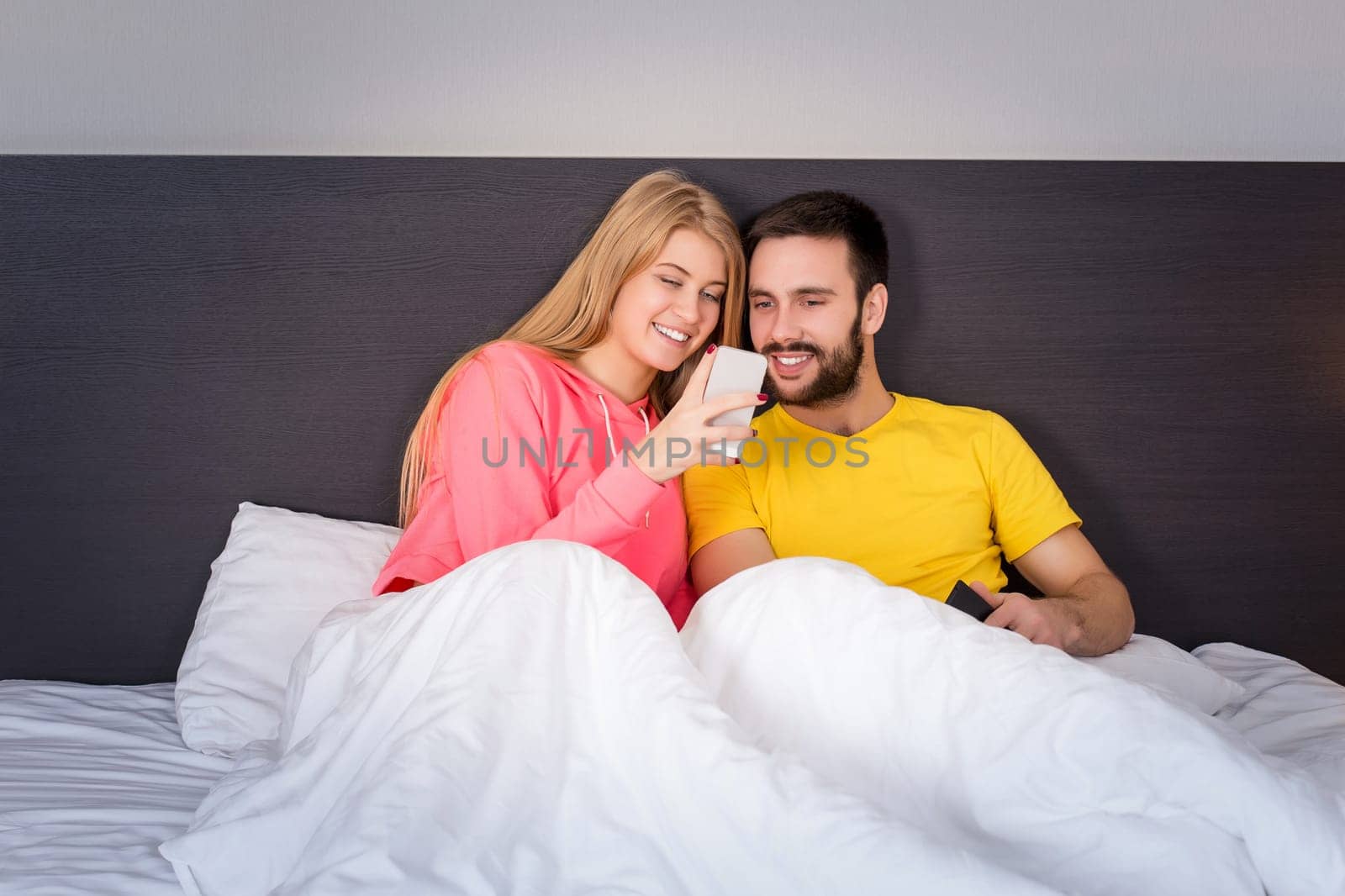 Young sweet couple at bed looking at a mobile phone. Concept about technology and people