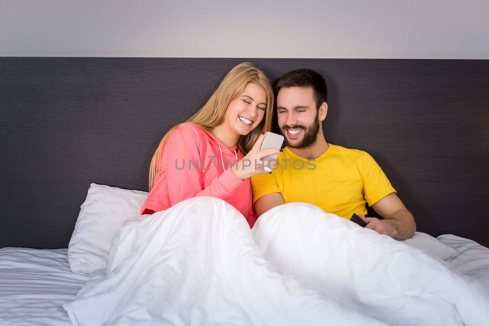 Young sweet couple at bed looking at a mobile phone. Concept about technology and people
