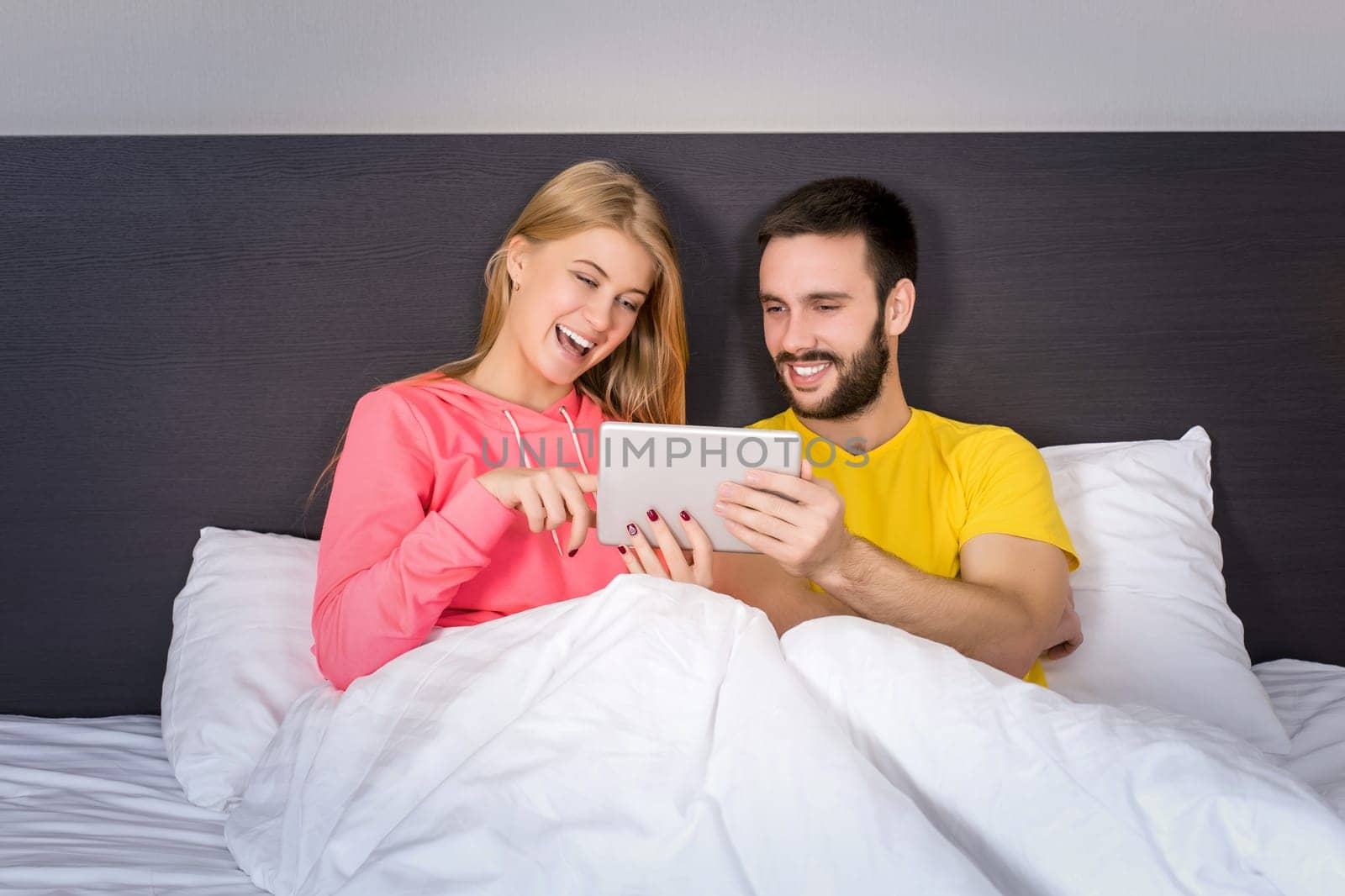 Young Sweet Couple on Bed Watching Something on Tablet Gadget. Concept about technology and people
