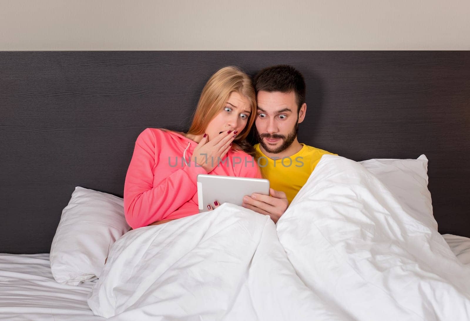 Young Sweet Couple at Bed Watching Something on Tablet Gadget by nazarovsergey