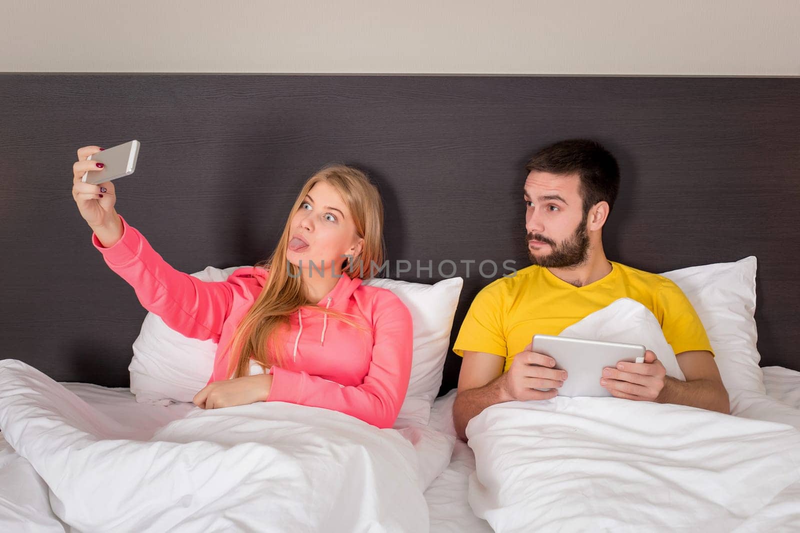 Young happy couple on bed doing selfie with telephone camera. Concept about technology and people