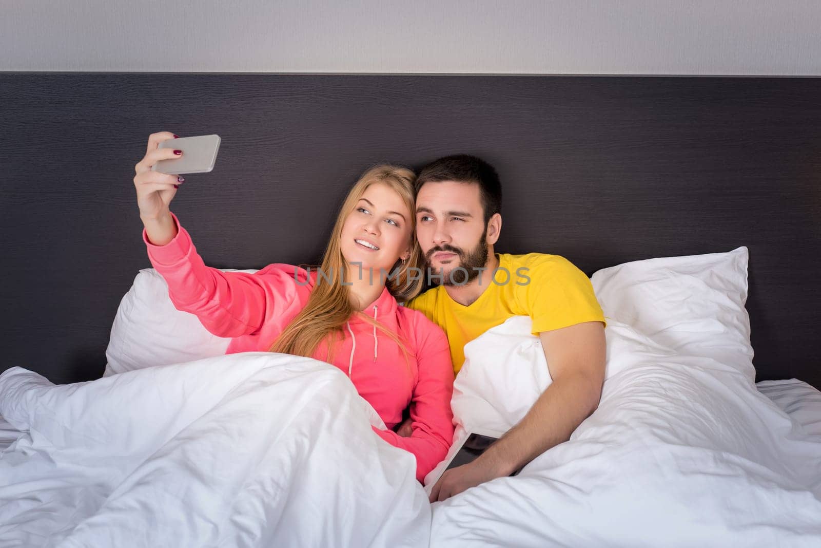 Young happy couple on bed doing selfie with telephone camera. Concept about technology and people