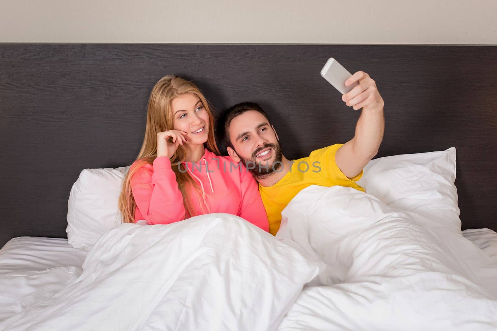 Young happy couple on bed doing selfie with telephone camera. Concept about technology and people