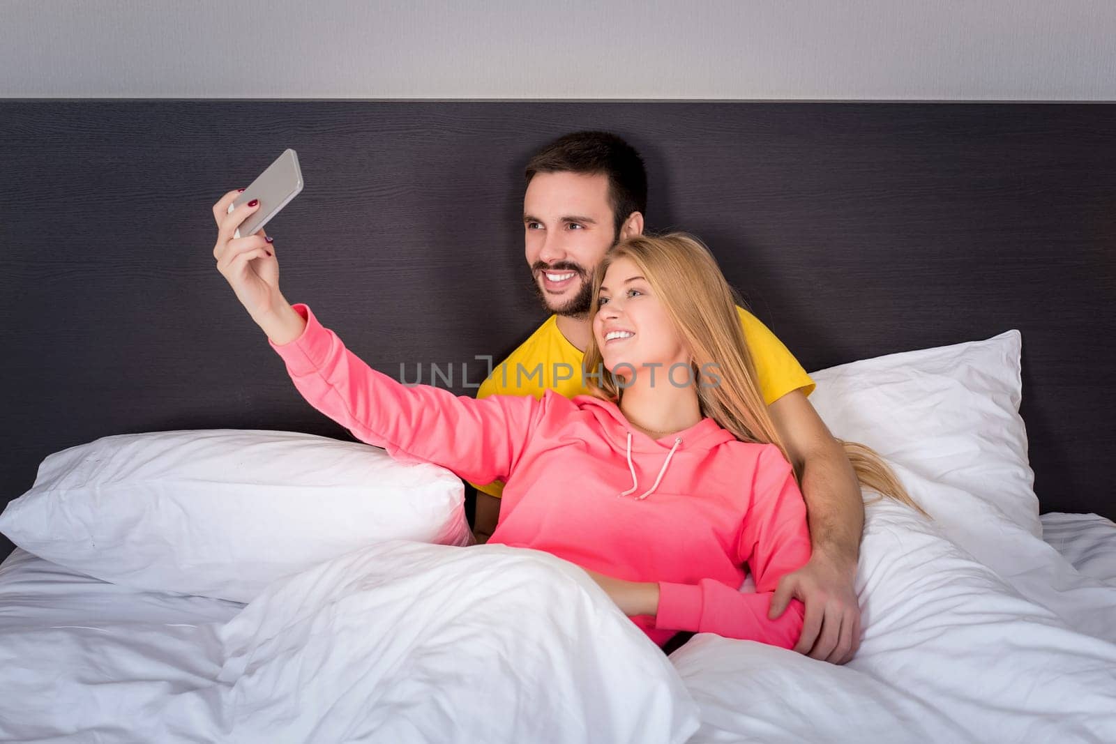 Young happy couple on bed doing selfie with telephone camera. Concept about technology and people