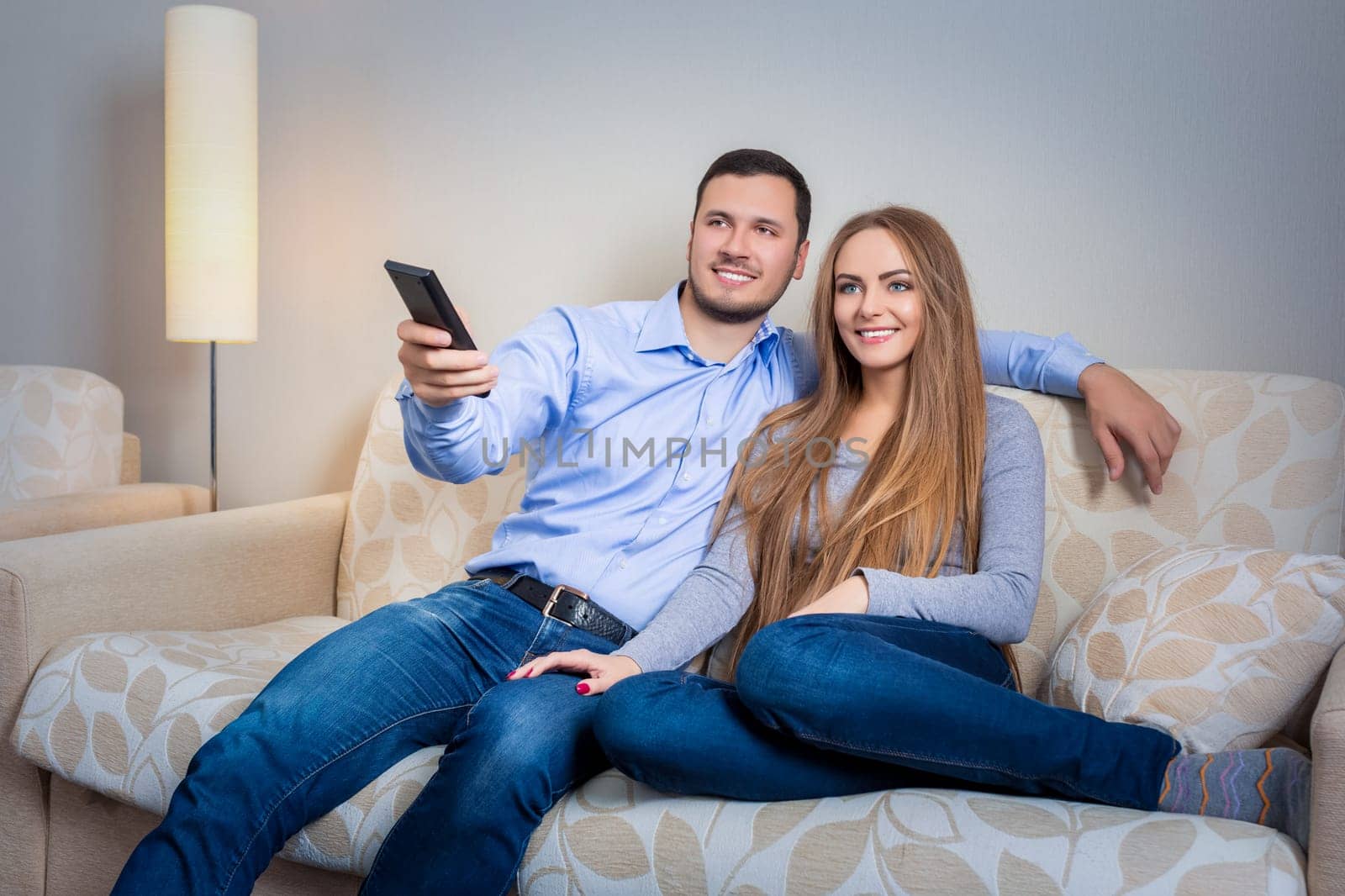 Happy couple sitting on sofa with remote control in hands and watching television together