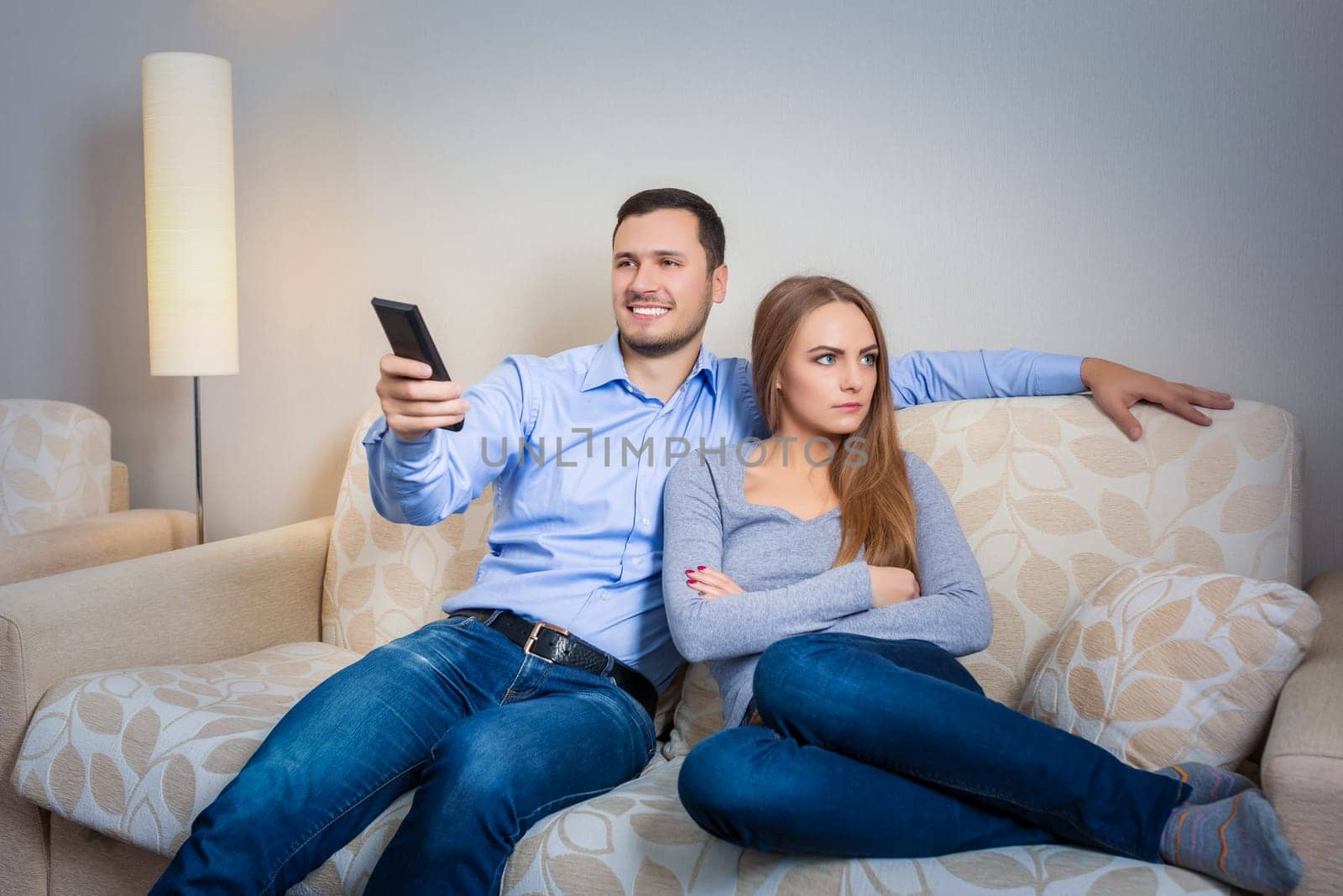 Portrait of couple sitting on sofa watching television. Image of hapy man with remote control in hands and upset woman