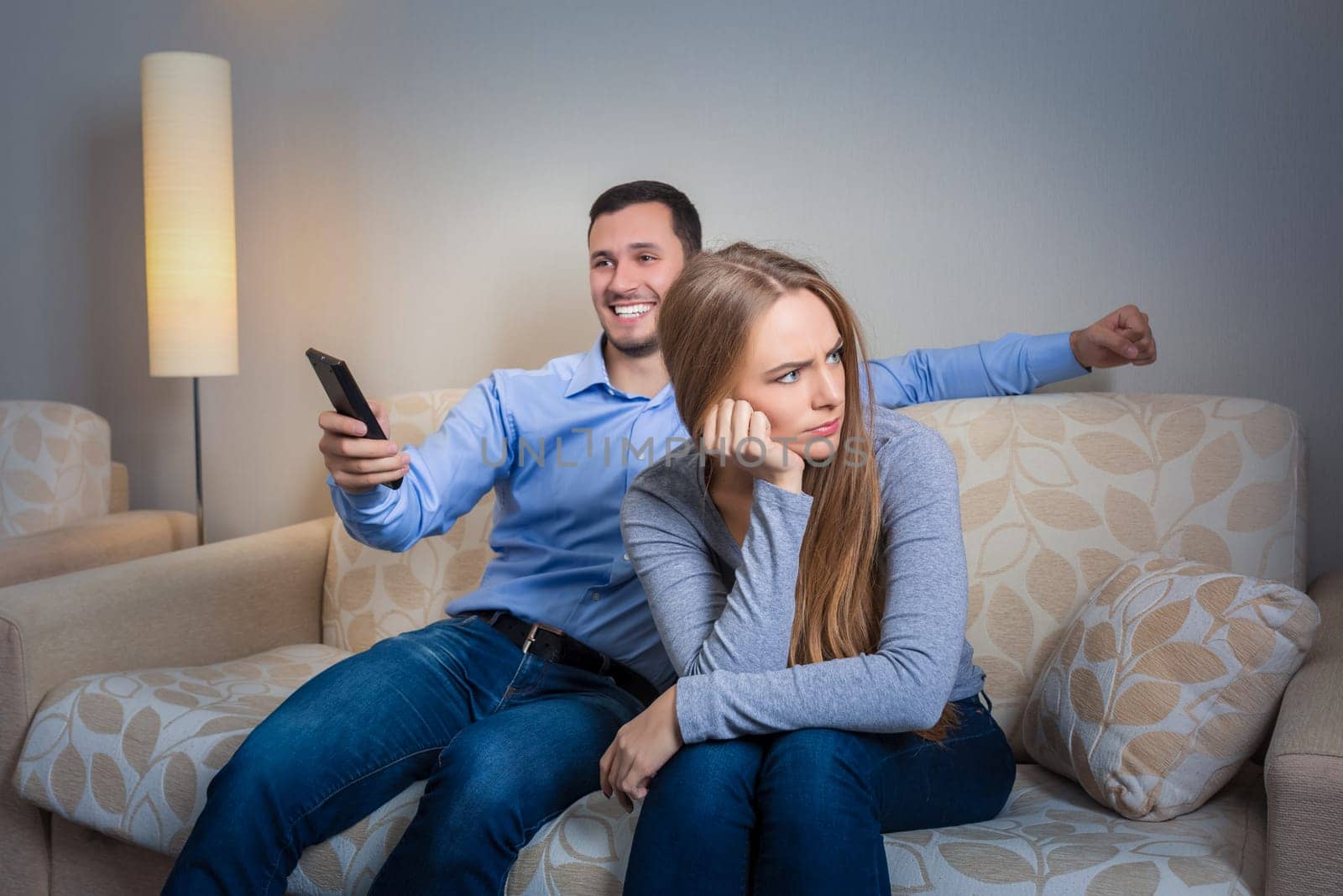 Portrait of couple sitting on sofa watching television. Image of hapy man with remote control in hands and upset woman