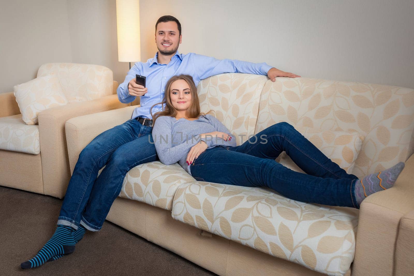 Portrait of happy couple sitting on sofa with remote control in hands and watching television together