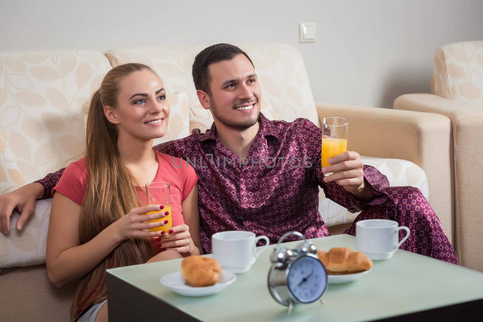 Cute young couple having breakfast, eating croissants, drinking orange juice. by nazarovsergey