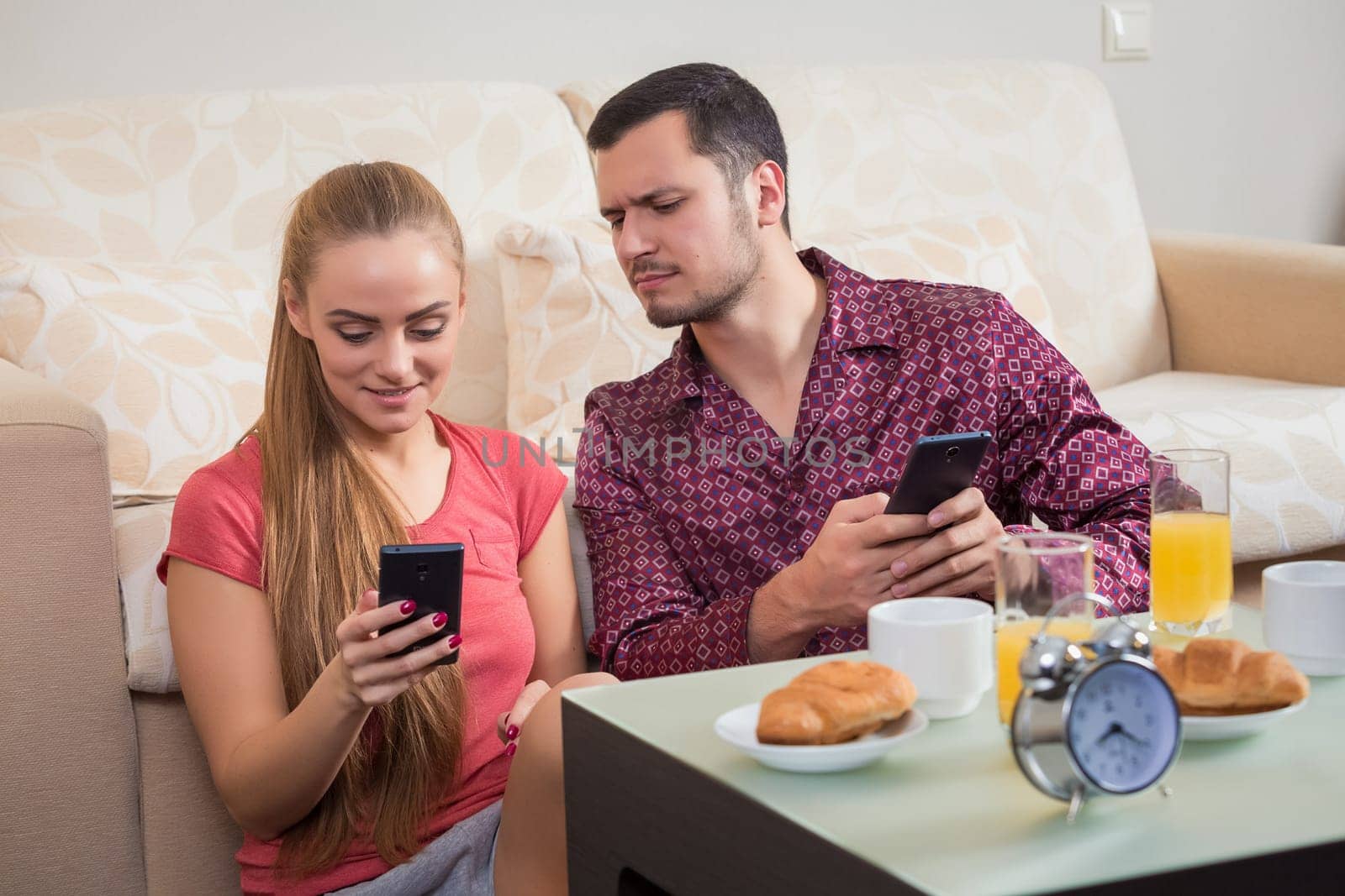 Cute young couple having breakfast and looking at mobile phone by nazarovsergey