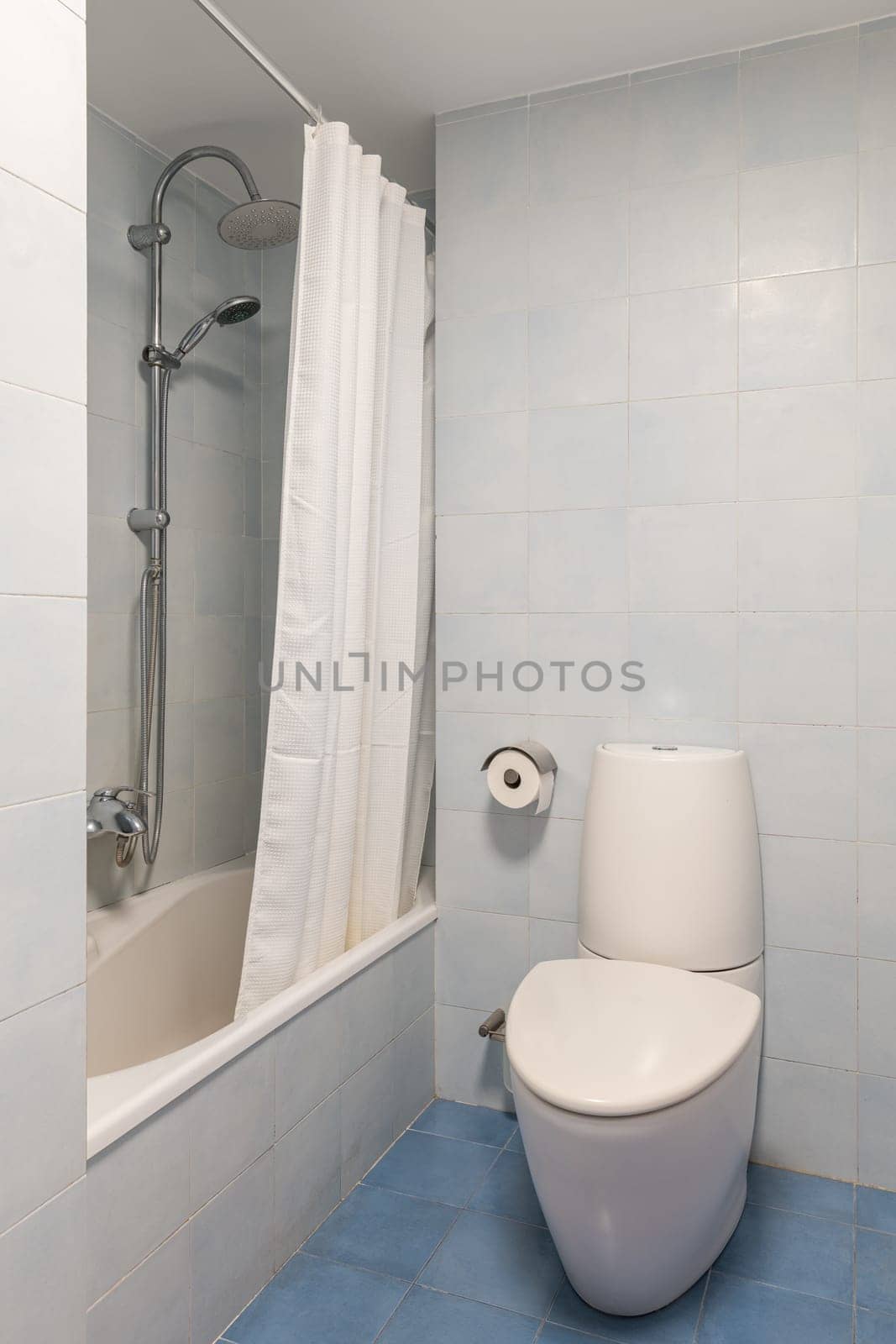 Toilet bowl near bathtub with shower in reconstructed bathroom. Equipment of personal hygiene in hotel room. Clean tiled restroom at home