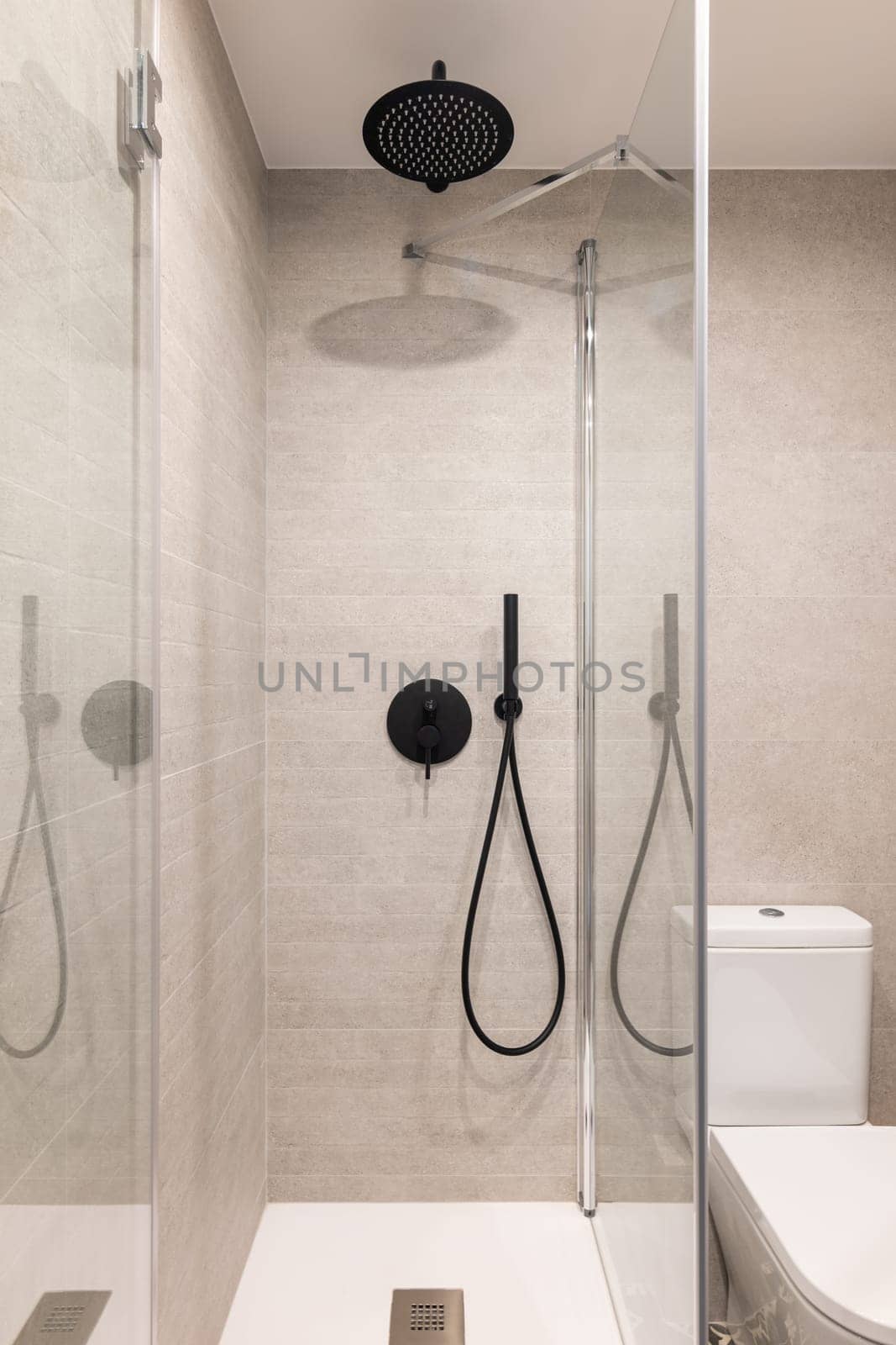 Glass shower unit and toilet bowl in stylish tiled bathroom. Equipment for personal hygiene in modern hotel room. Home interior design
