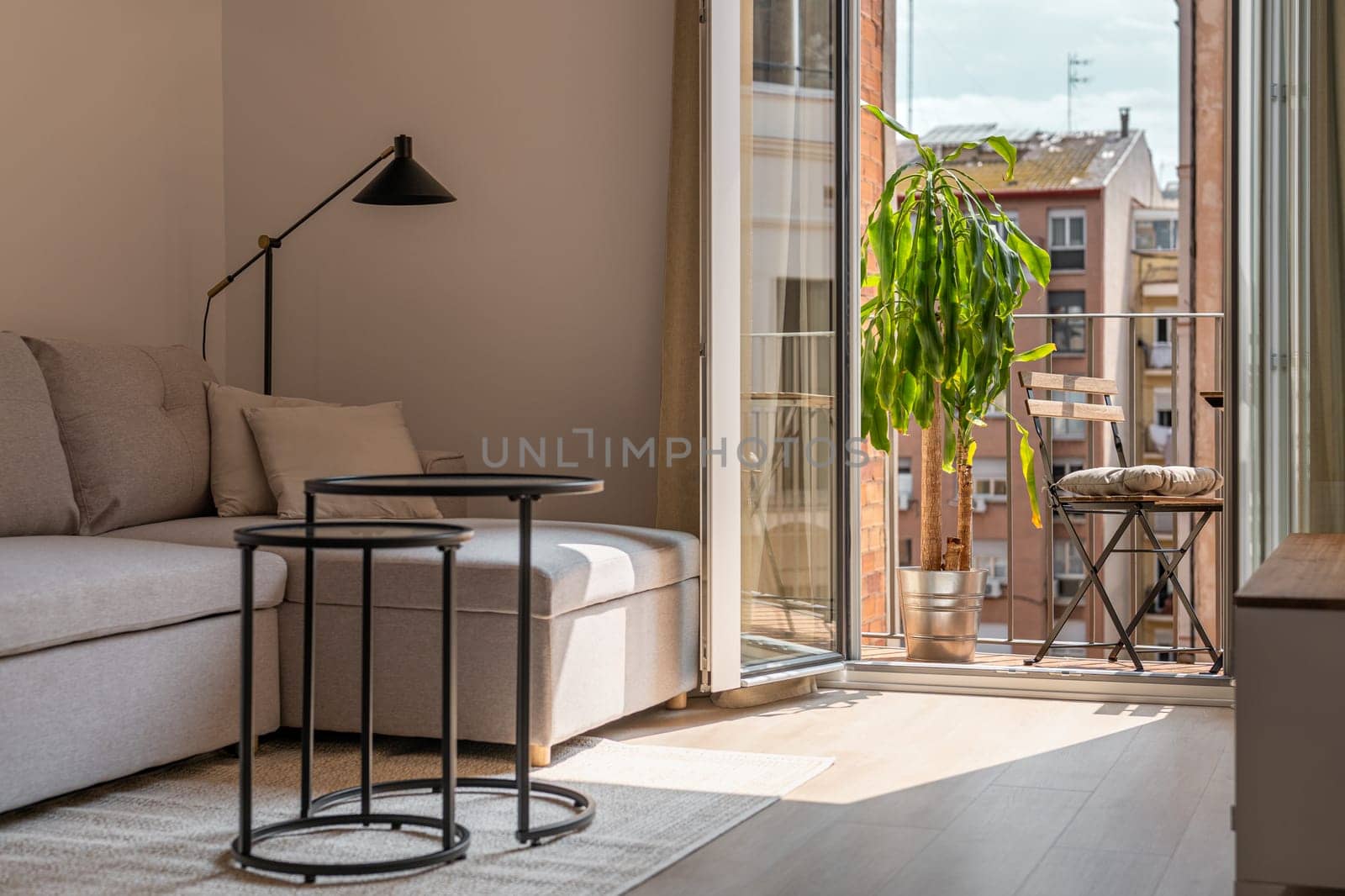 Shady living room and open balcony door in studio apartment on sunny day. Residential house interior with stylish furniture in Barcelona